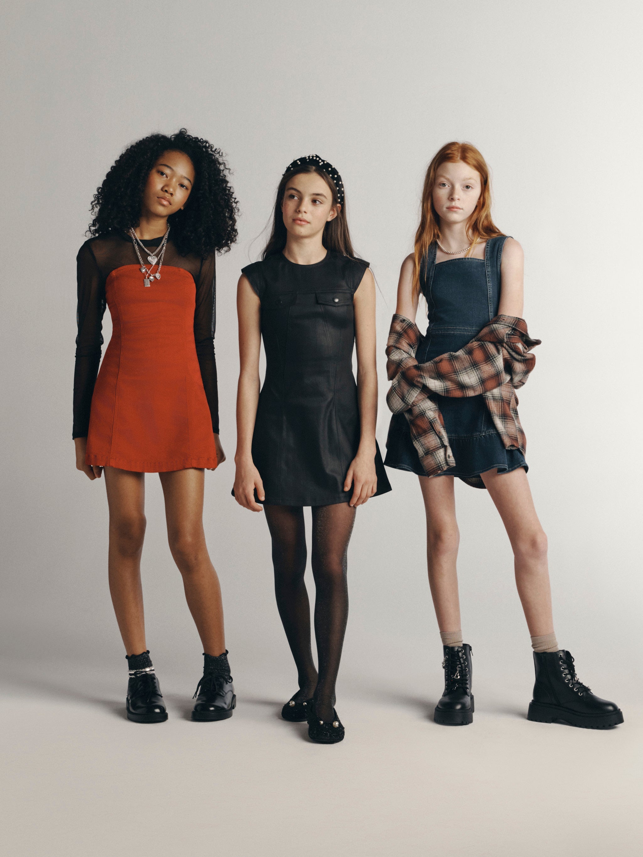 DL1961 girls' Fall 26 group shot of three girls; at left, the rust Bety Strapless Dress over a black mesh top, studio.