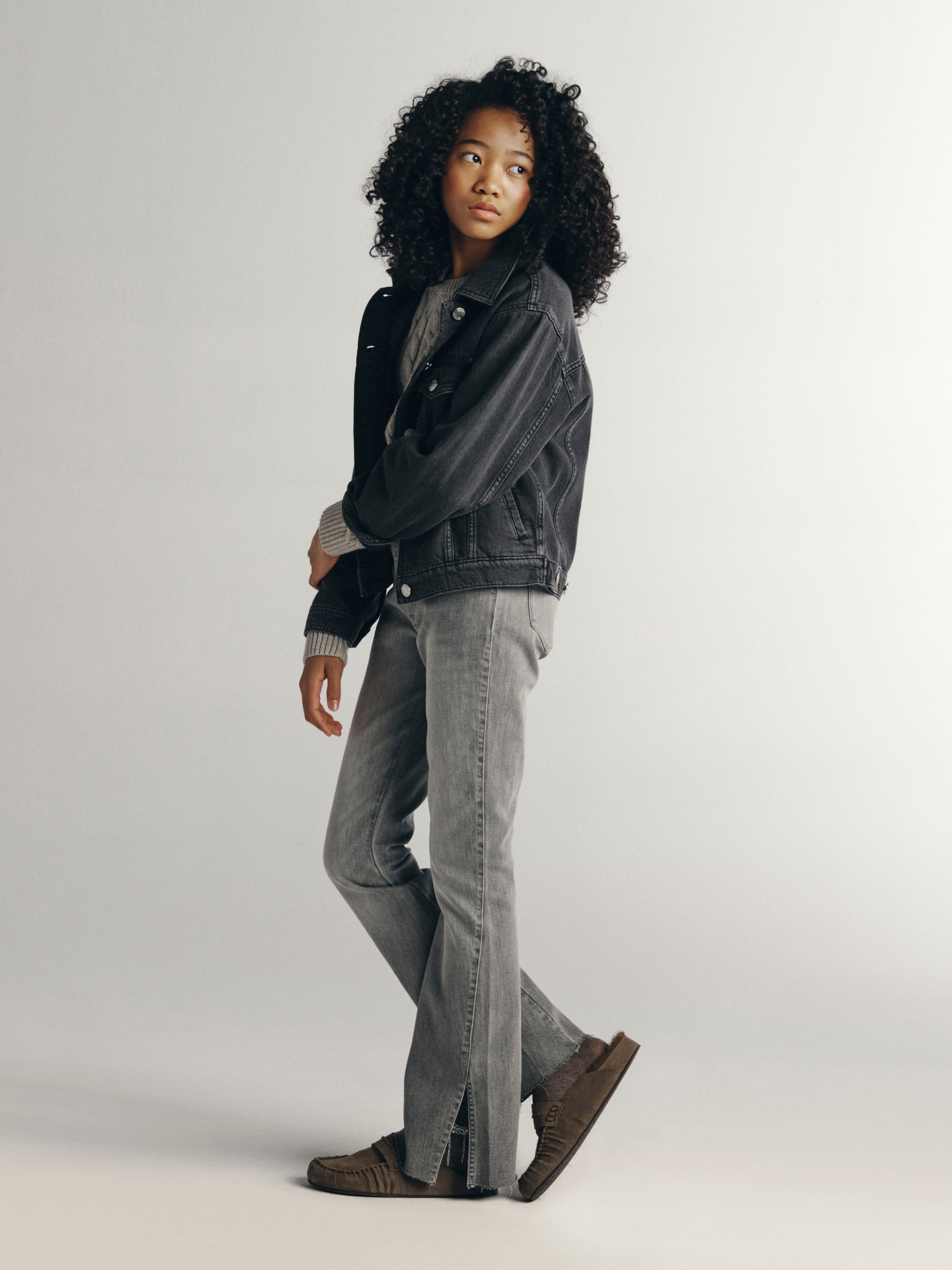 DL1961 Kids girls' Claire bootcut jeans in Twister with a grey Jordyn trucker jacket, full-length side profile in a studio.