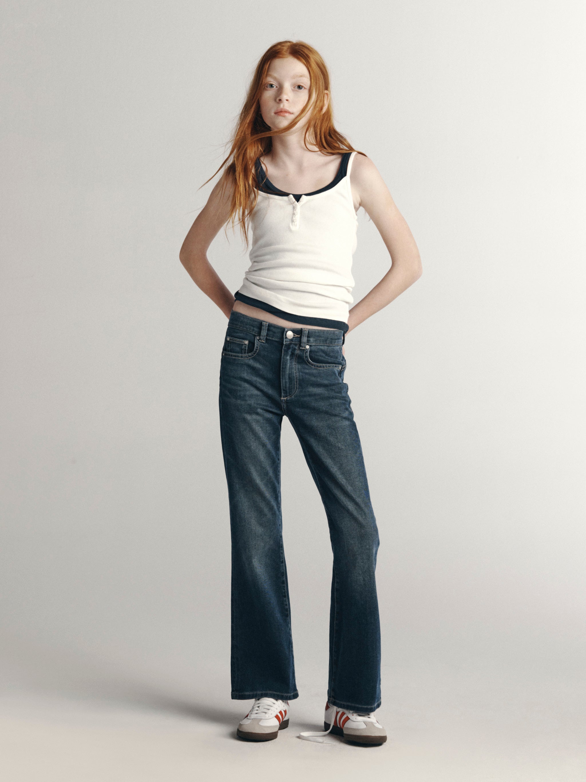 DL1961 Kids girls' Cleo bootcut jeans in Nightlight with a white ribbed tank and sneakers, full-length front, studio.