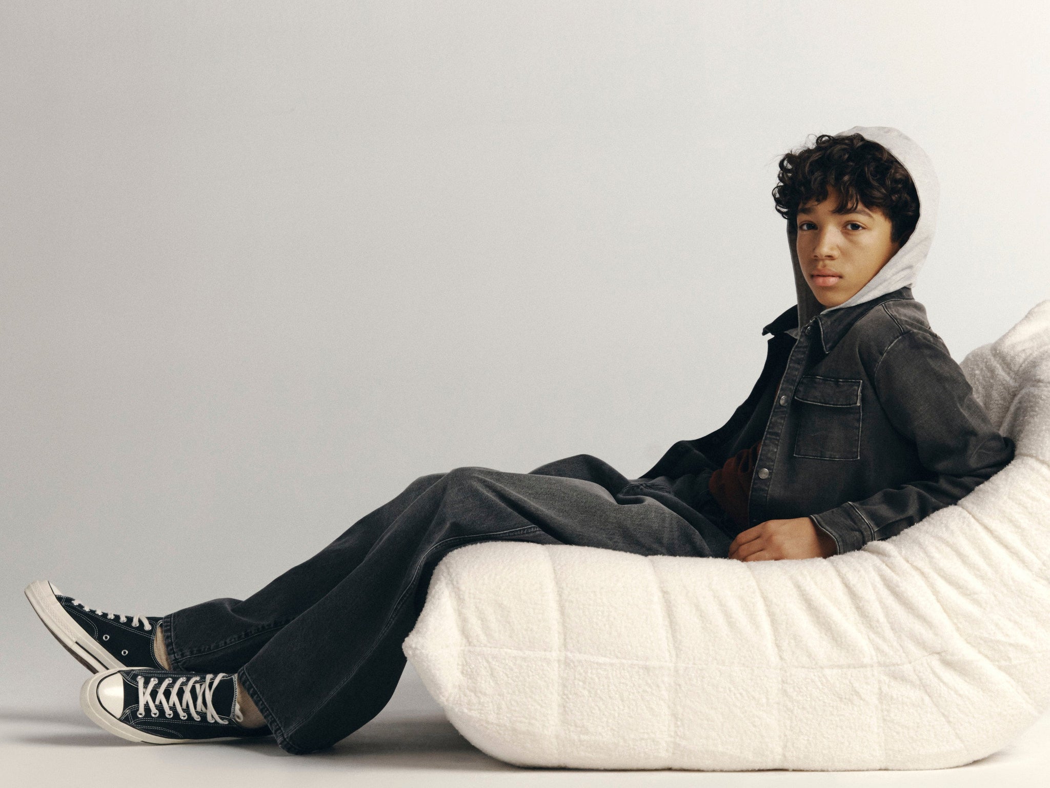 DL1961 Kids boys' Mason wide-leg jeans in Nightshade with a grey Matteo hooded shirt, reclining full-length in a studio.