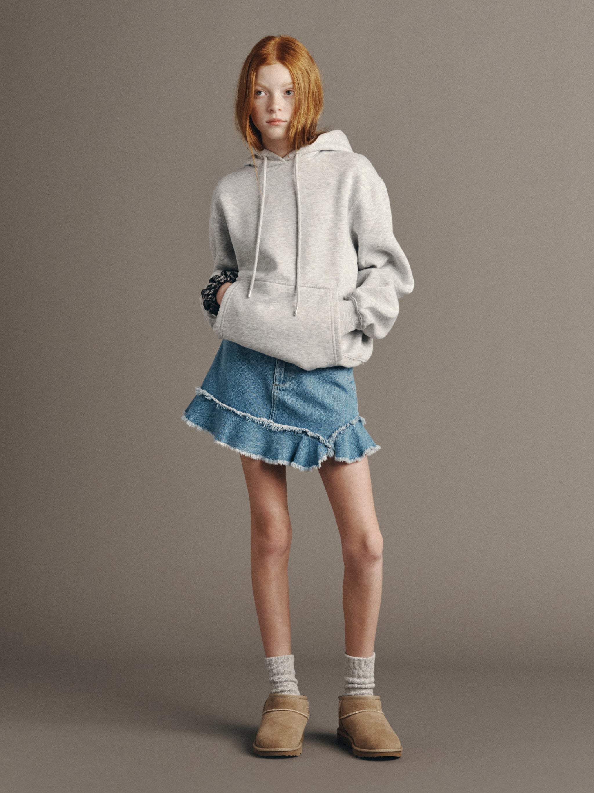 DL1961 Kids girls' Jenny ruffle denim skirt in Unraveled with a grey hoodie, full-length front, studio.
