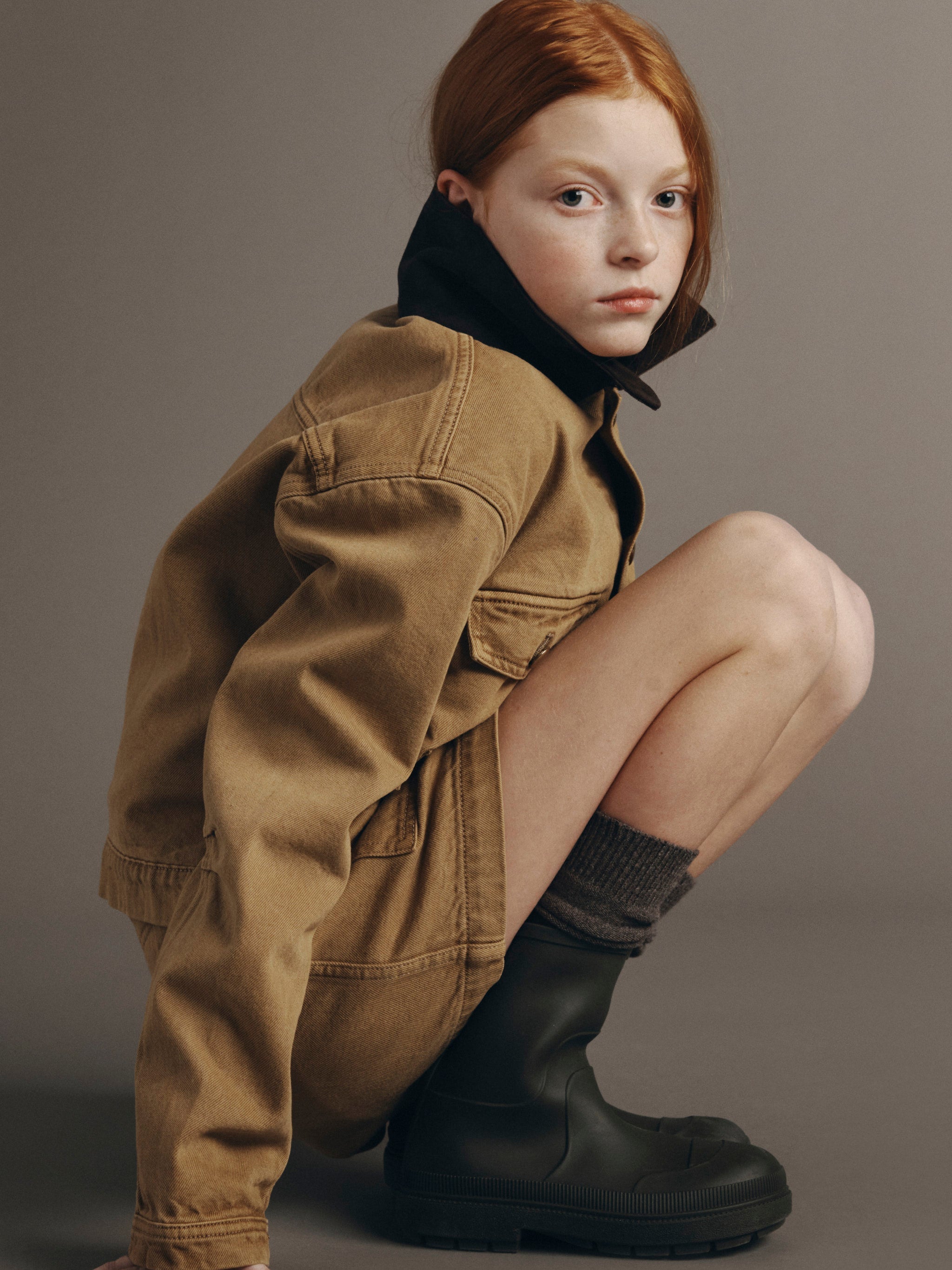 DL1961 Kids girls' Selina skirt in Savannas with a matching Reese utility jacket, crouching three-quarter view in a studio.