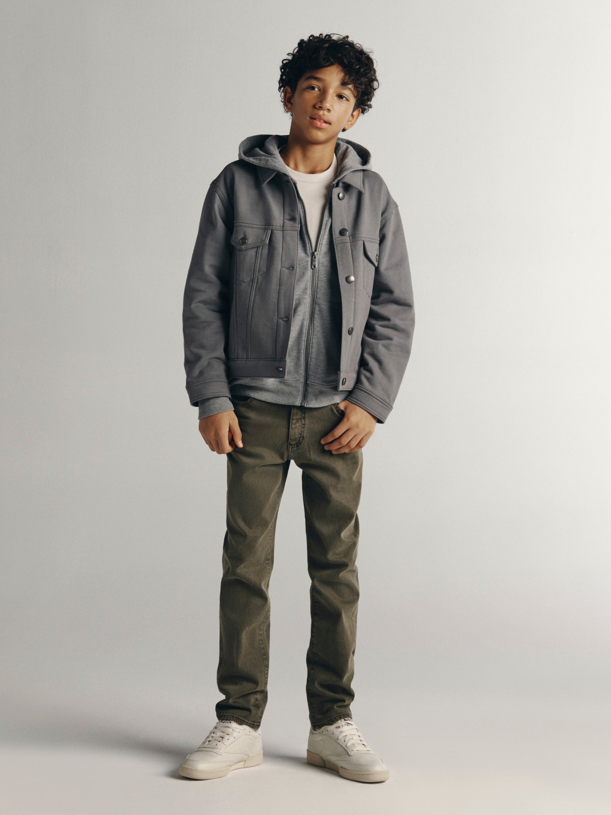 DL1961 Kids boys' Brady slim jeans in Outpost with a grey Jordyn hooded trucker jacket and white sneakers, full-length front, studio.
