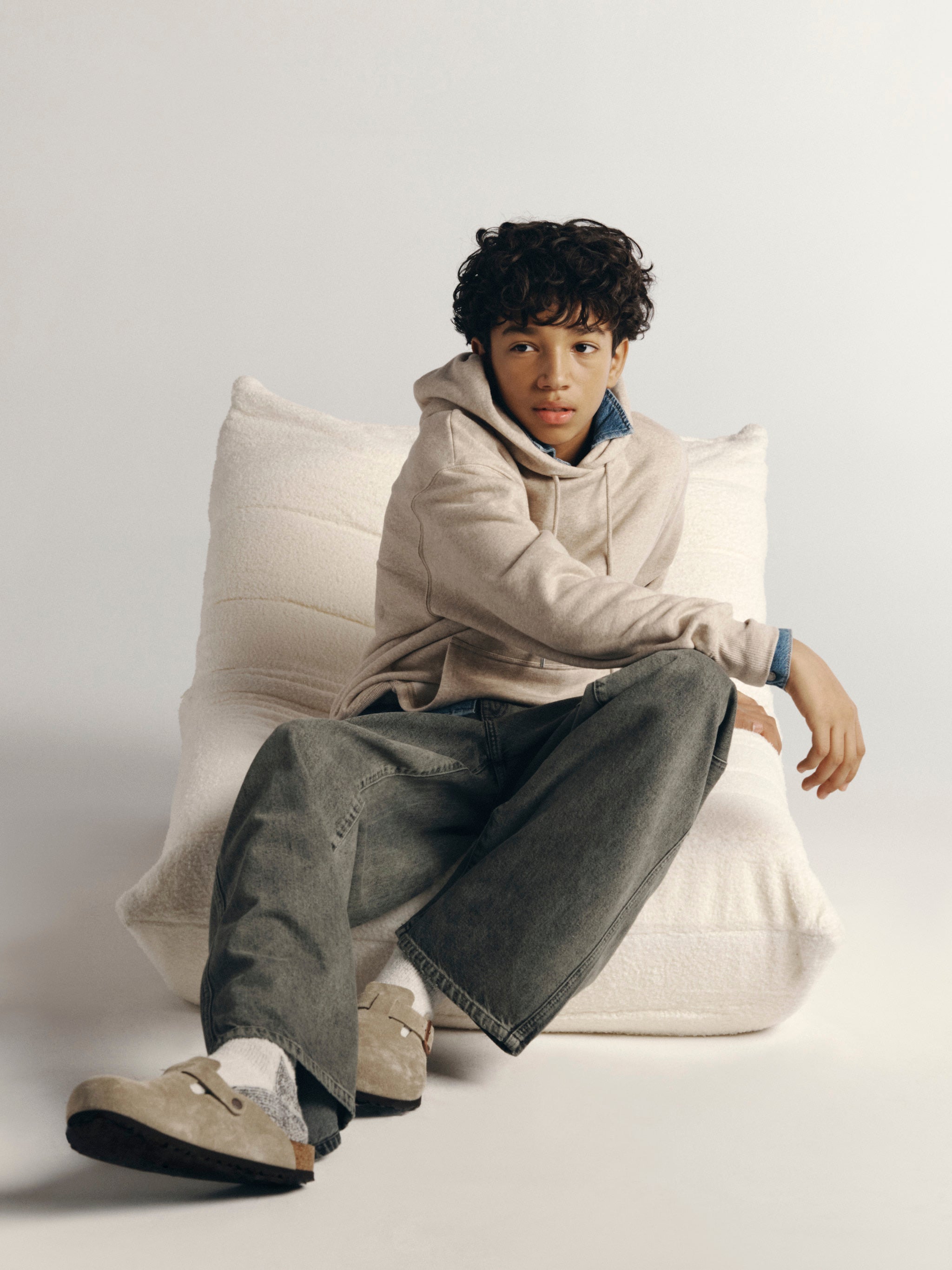 DL1961 Kids boys' Mason wide-leg jeans in Character Green with an oatmeal hoodie, seated full-length in a studio.