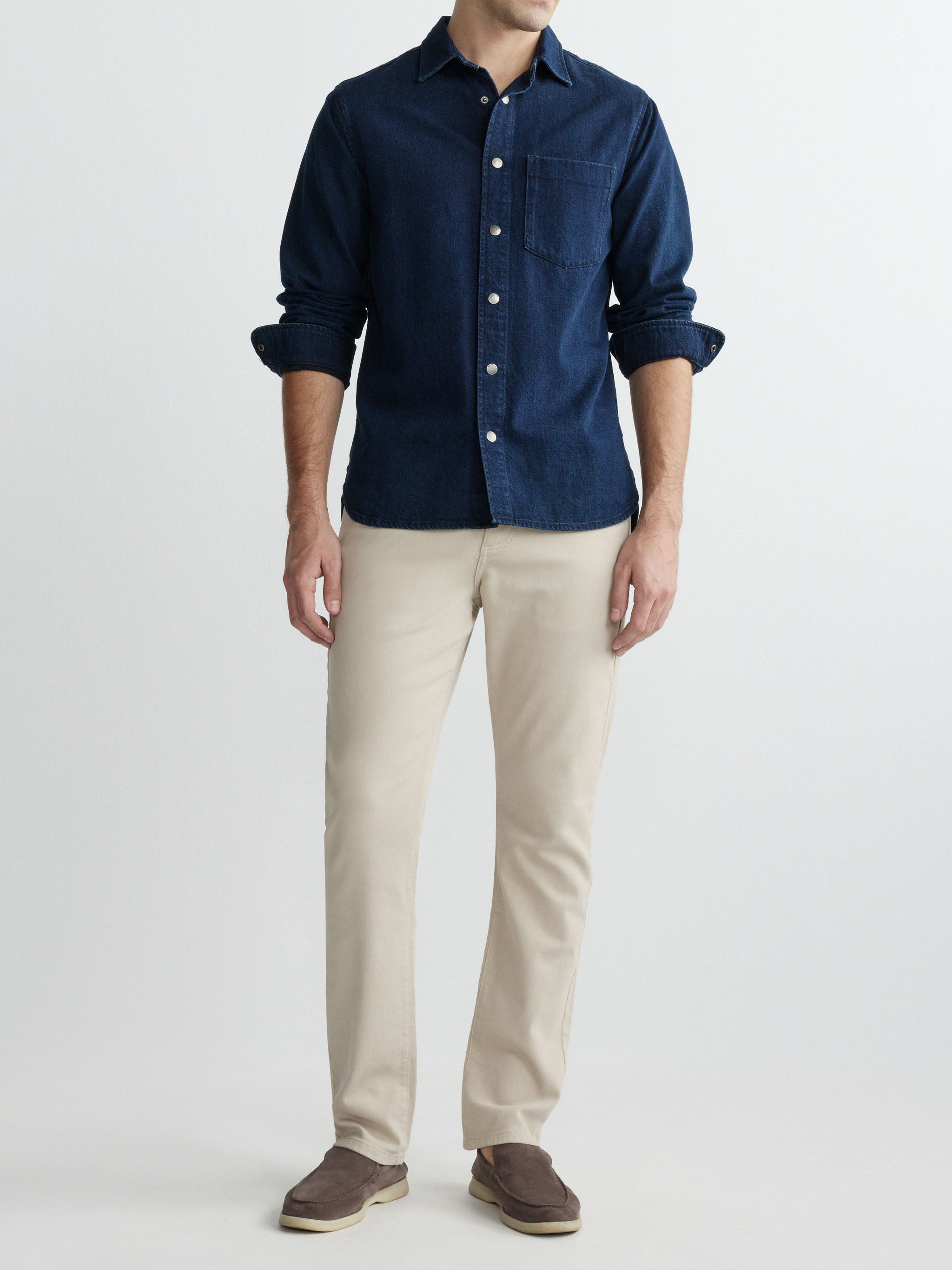 Person wearing a navy button-up shirt and beige pants on a white background