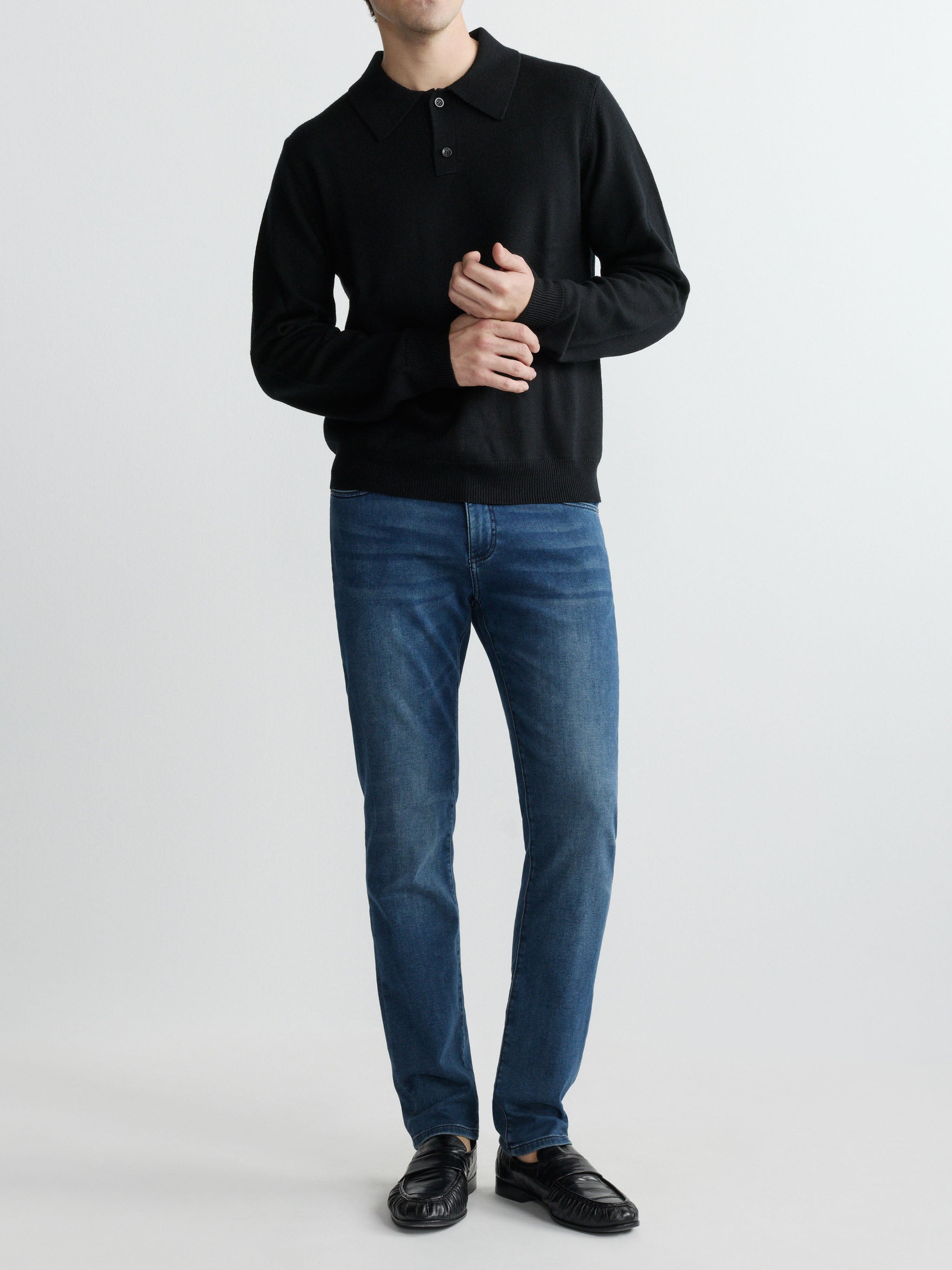 Person wearing a black long-sleeve shirt and blue jeans on a white background