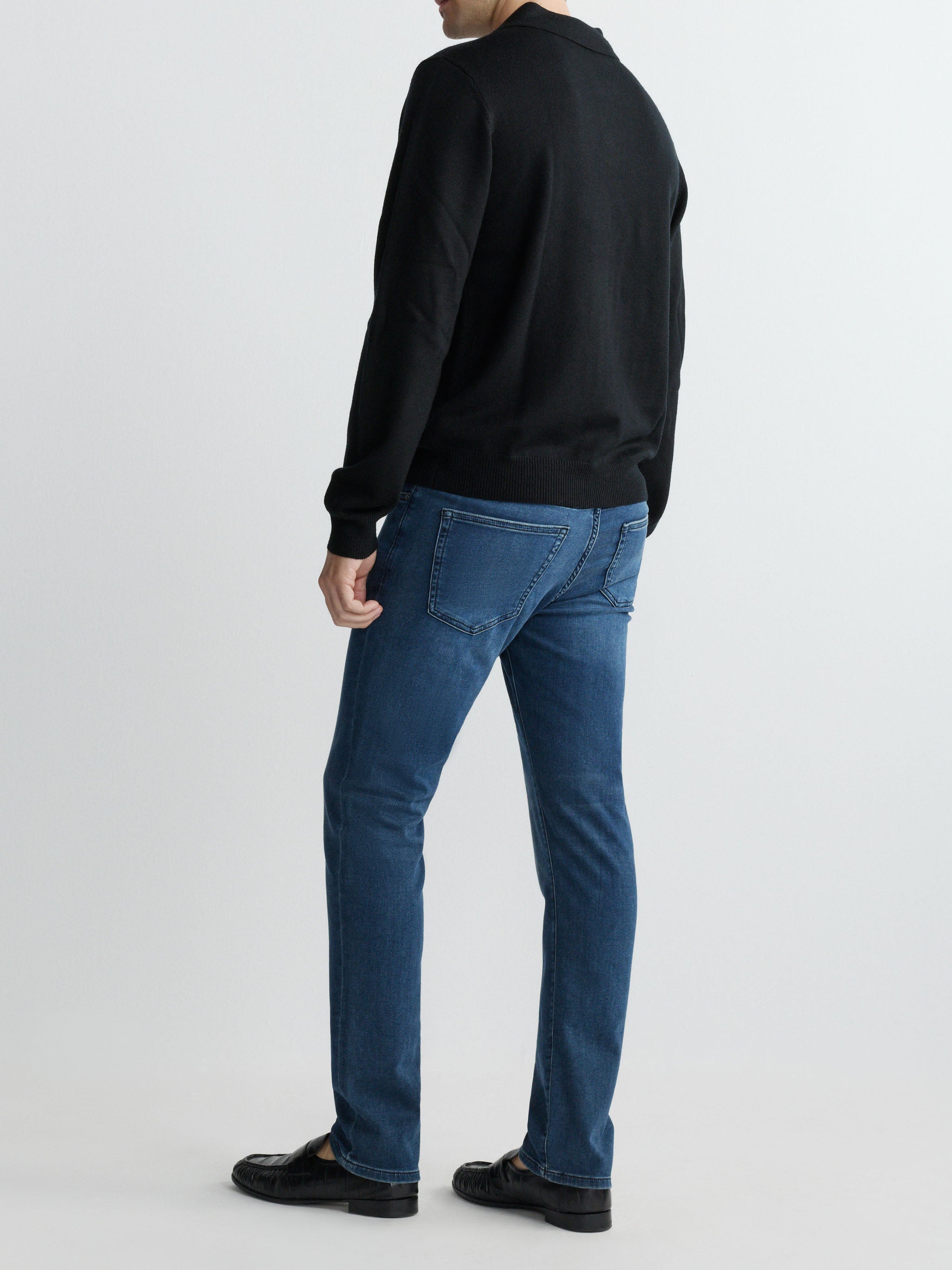 Person wearing a black sweater and blue jeans on a white background