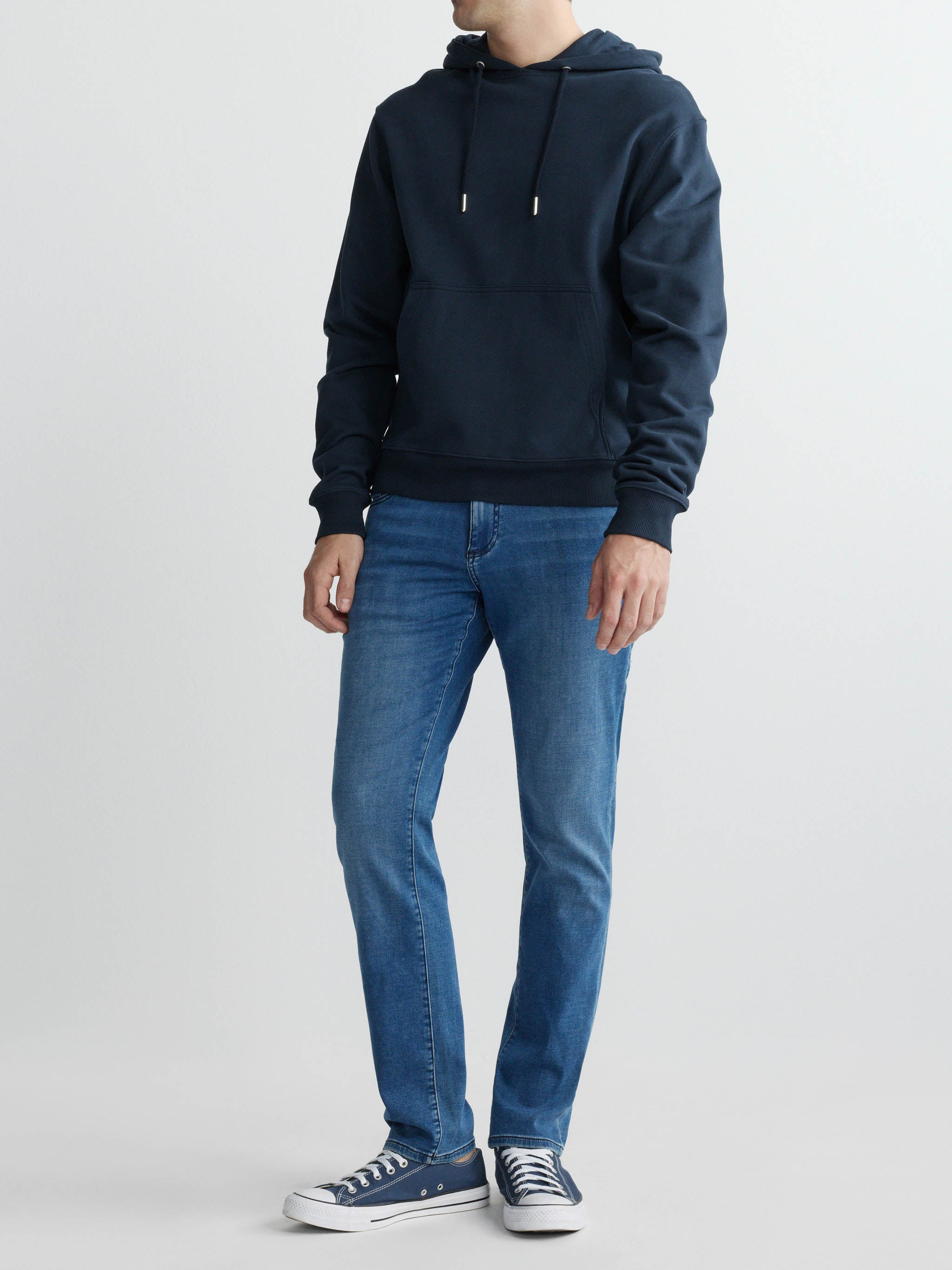 Person wearing a navy hoodie and blue jeans on a white background