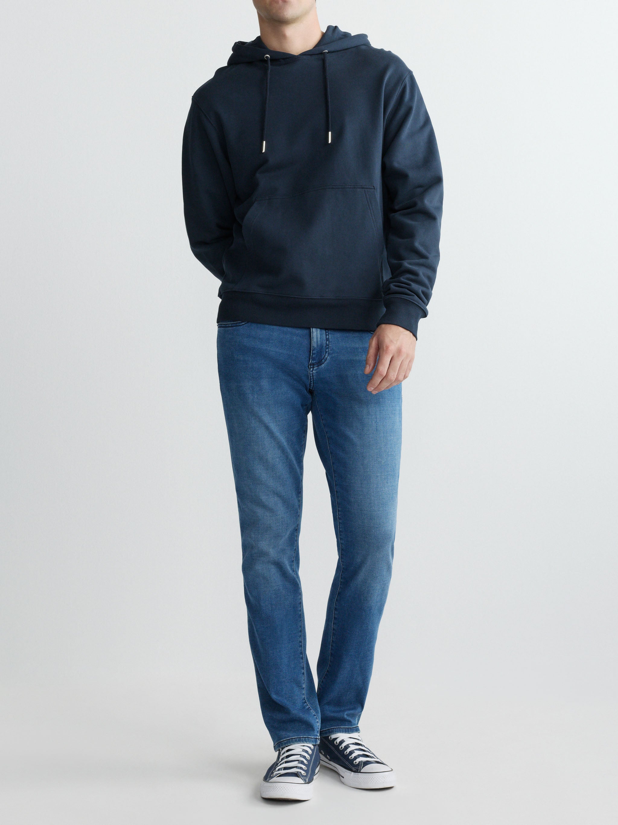 Person wearing a navy hoodie and blue jeans on a white background