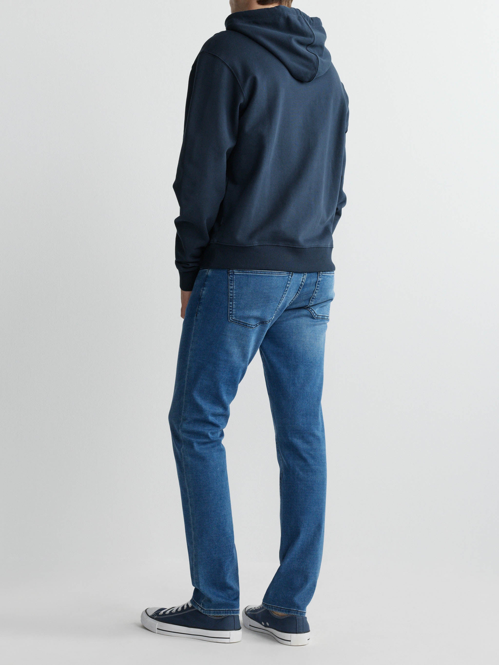 Person wearing a blue hoodie and jeans from behind on a white background