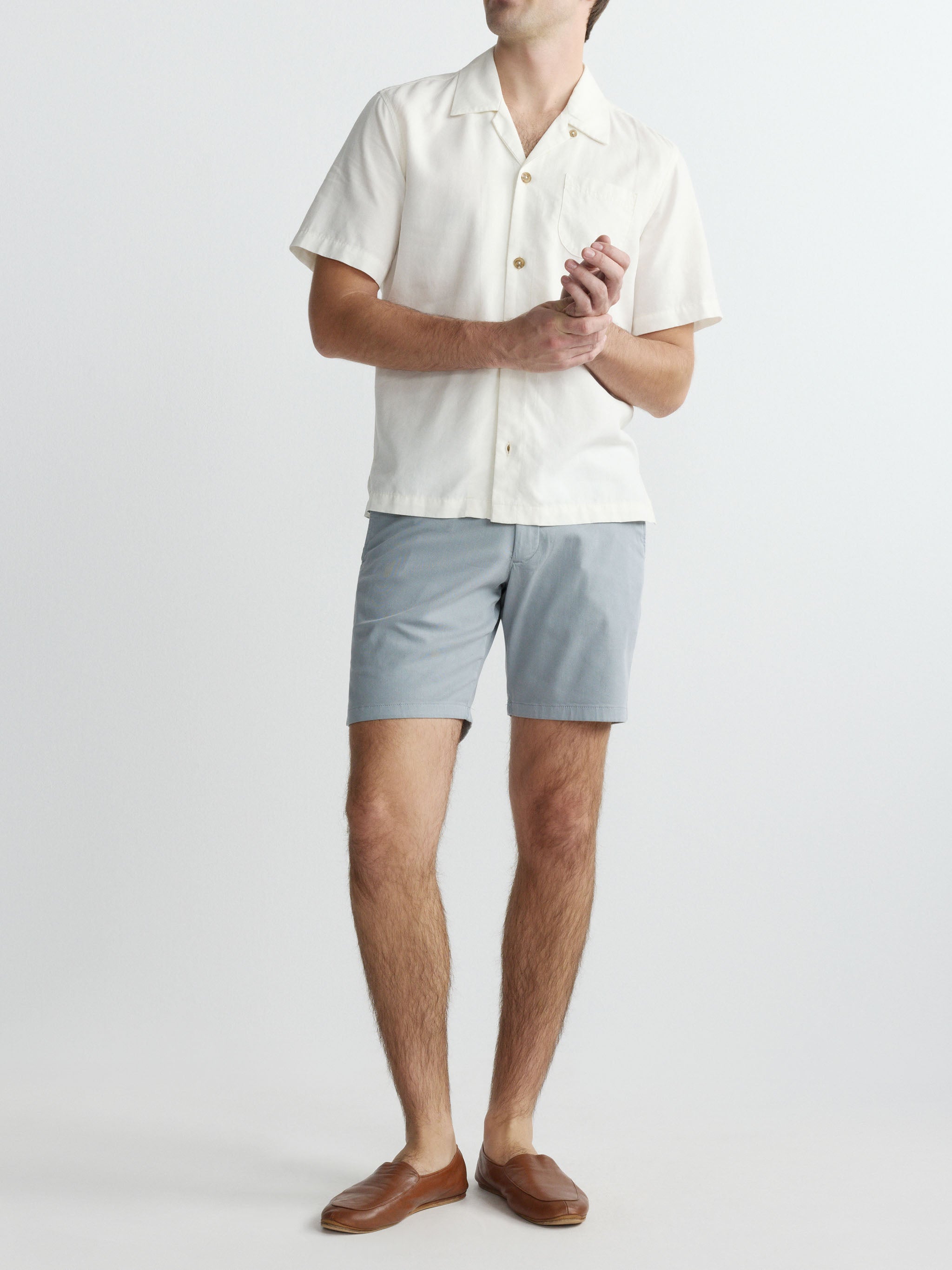 Person wearing a white shirt and light gray shorts on a plain background