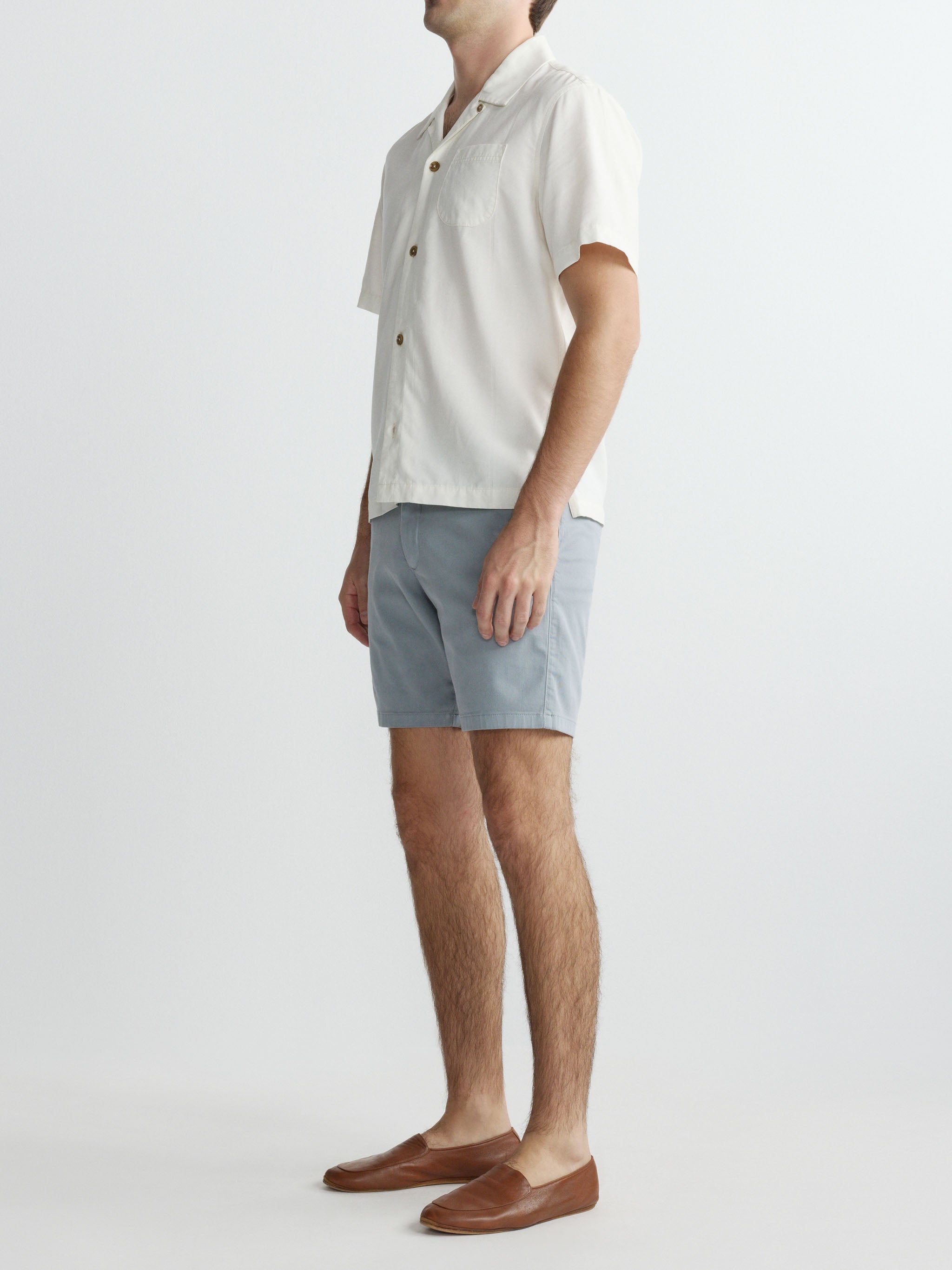 Man wearing a light-colored shirt and gray shorts on a white background