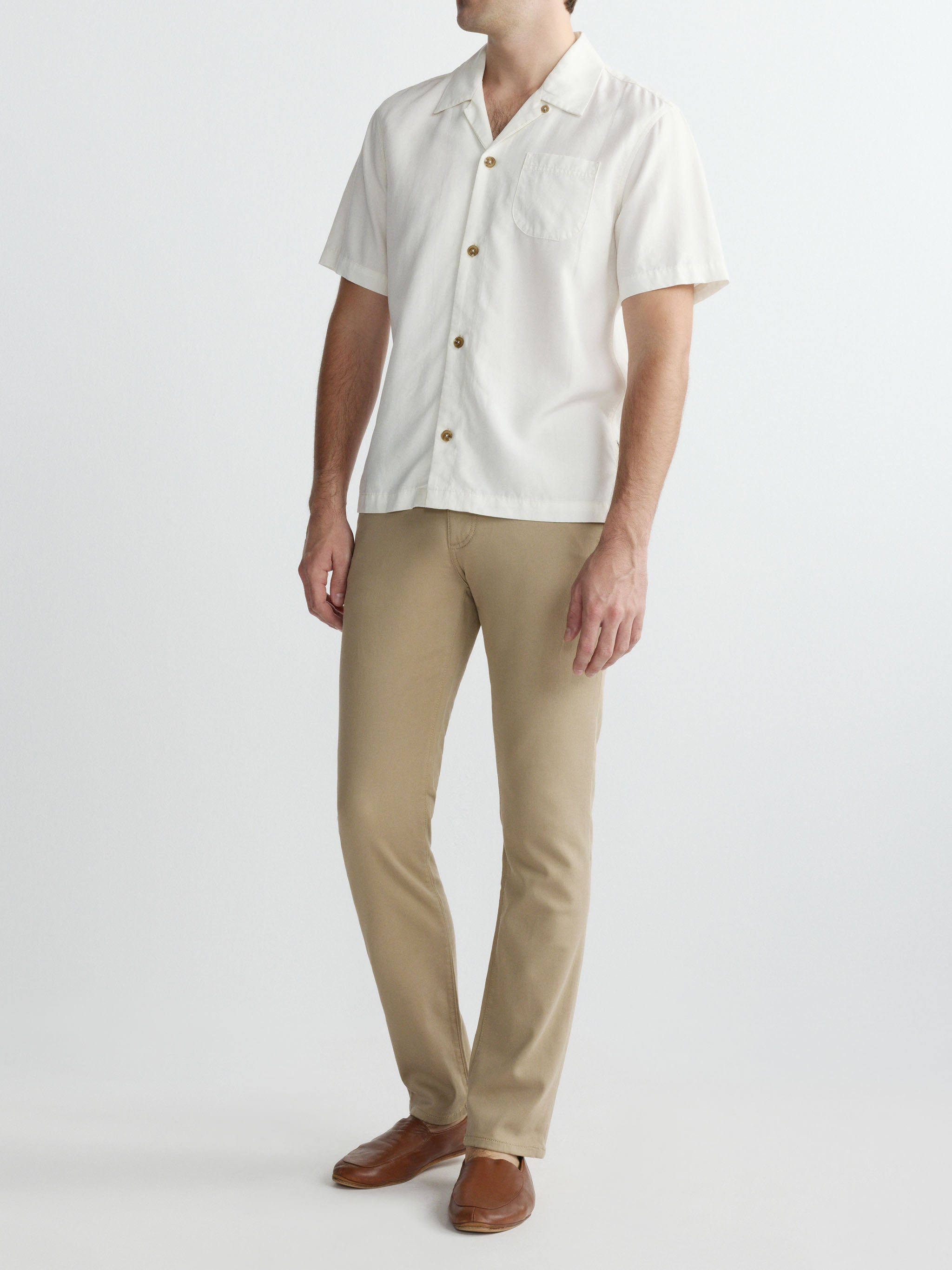 Person wearing a white short-sleeve shirt with buttons and beige pants on a white background