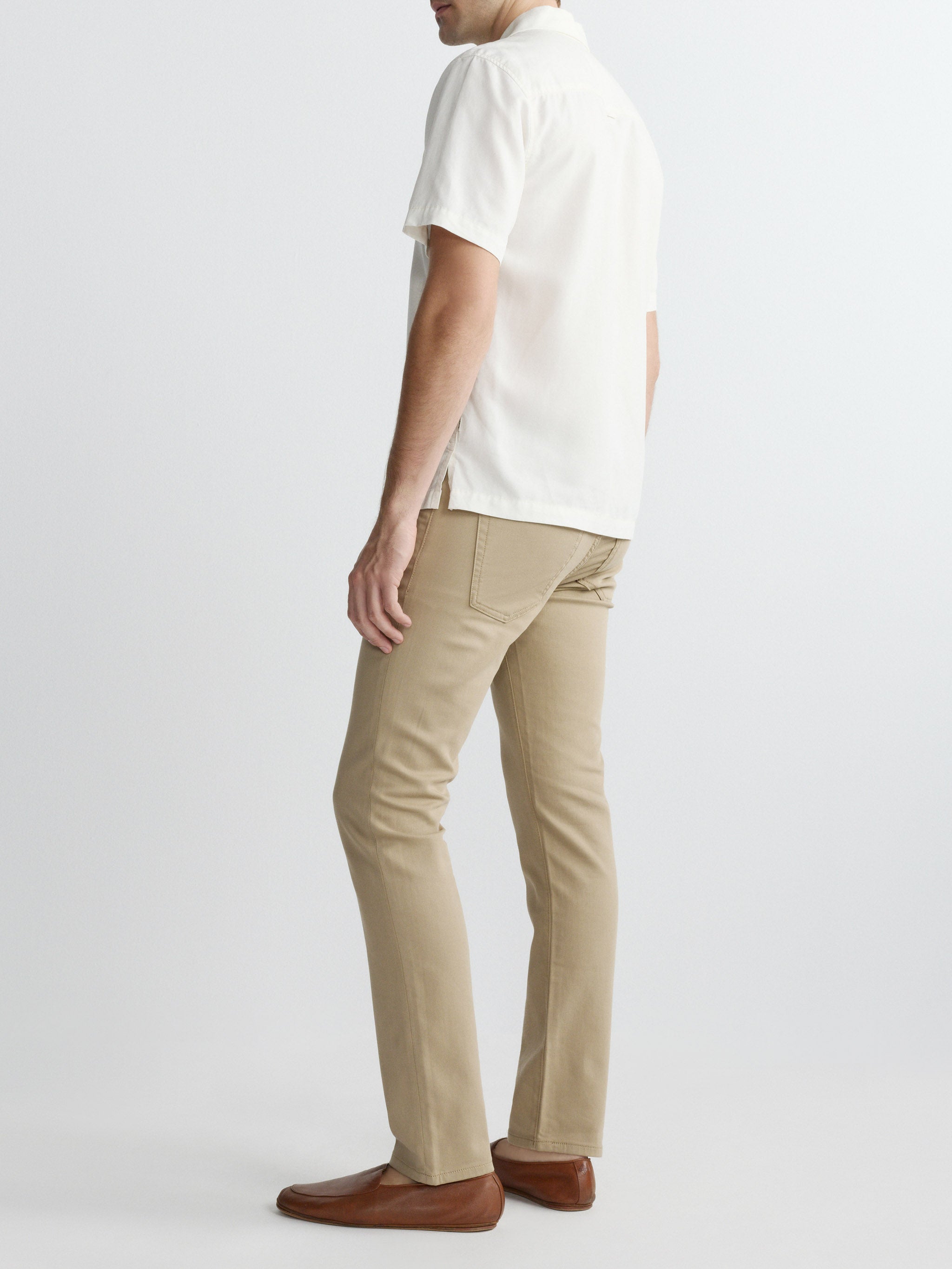 Man wearing a white shirt and beige pants on a plain background