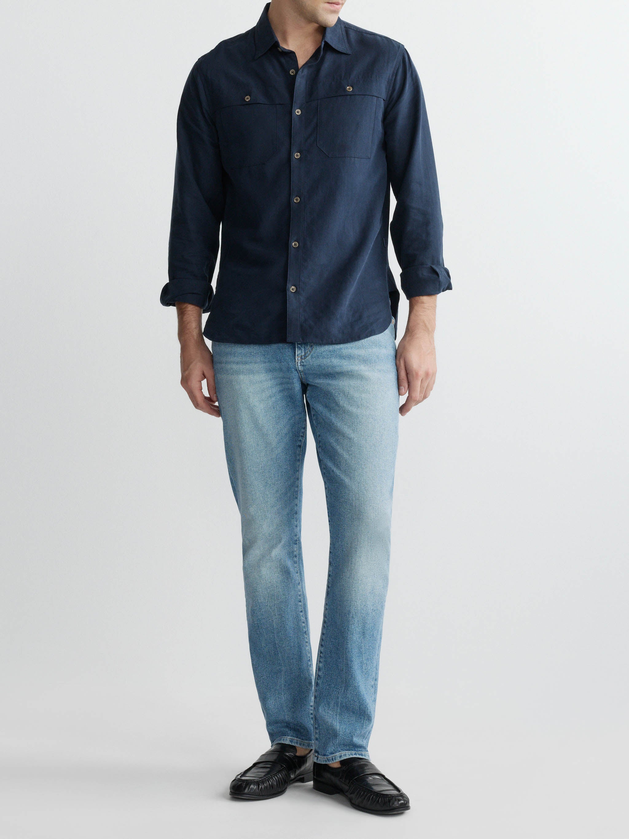 Man wearing a navy button-up shirt and light blue jeans on a white background