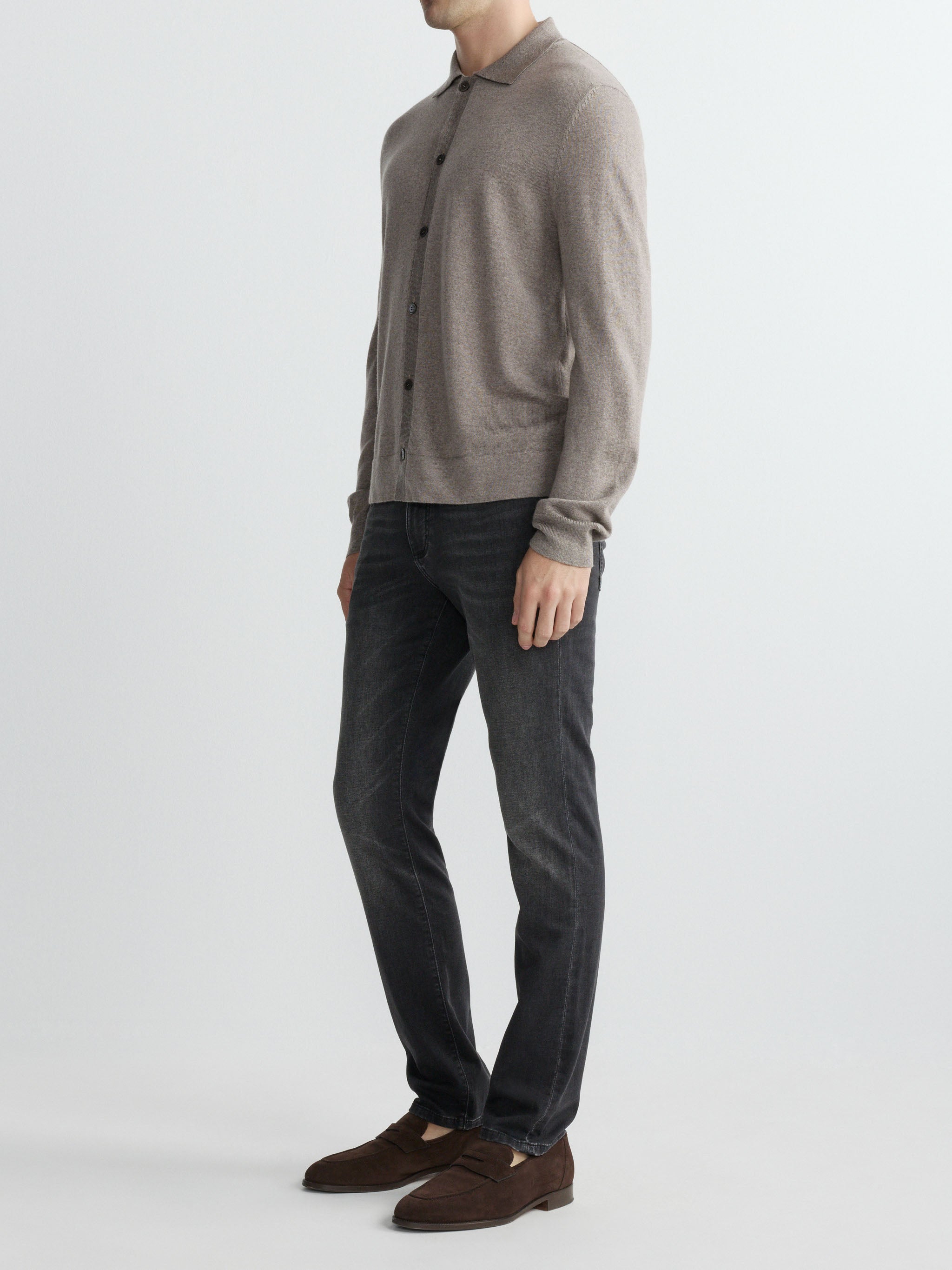 Person wearing a gray sweater, dark jeans, and brown shoes on a white background