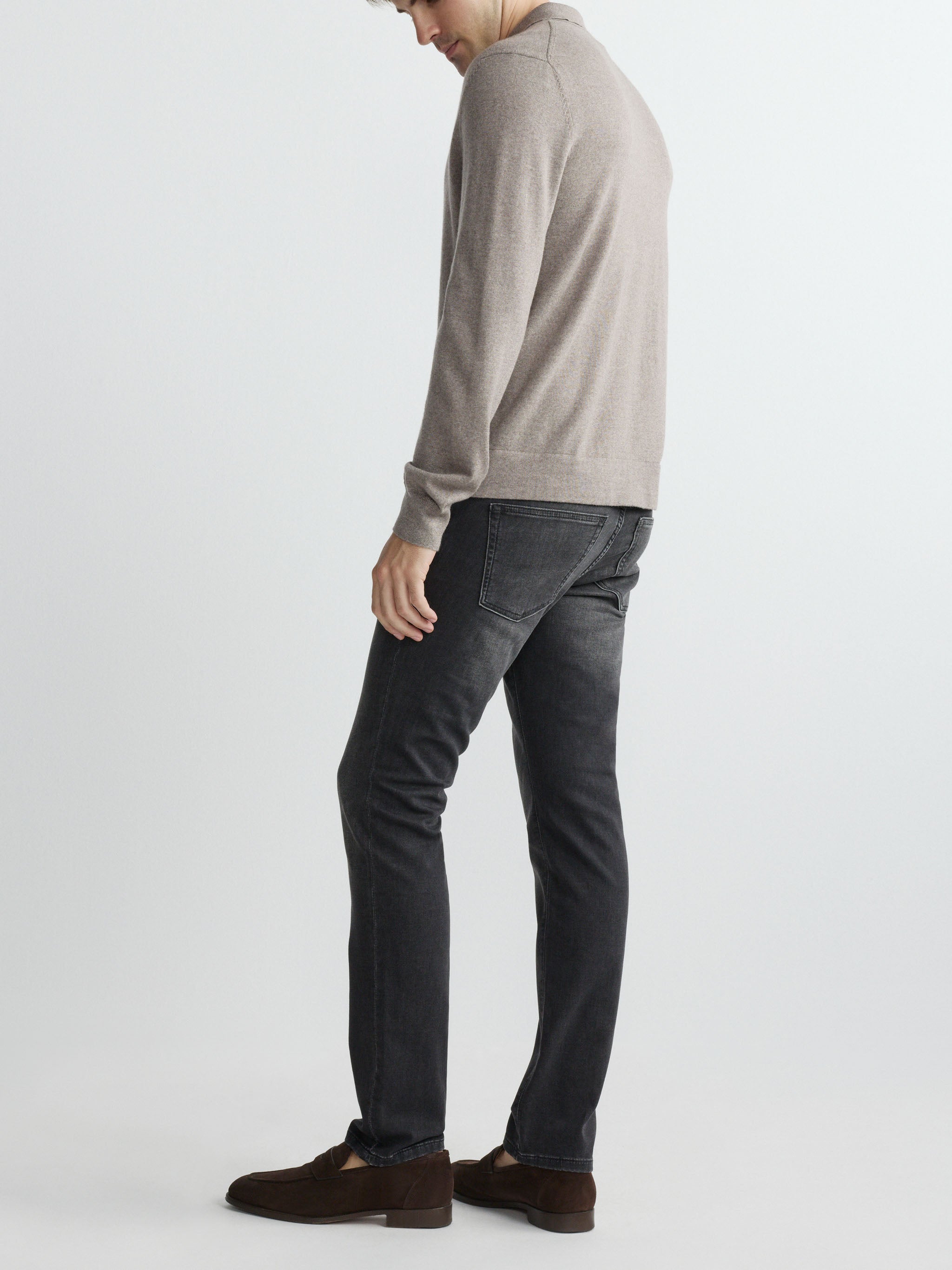 Person wearing a gray sweater and dark jeans on a white background