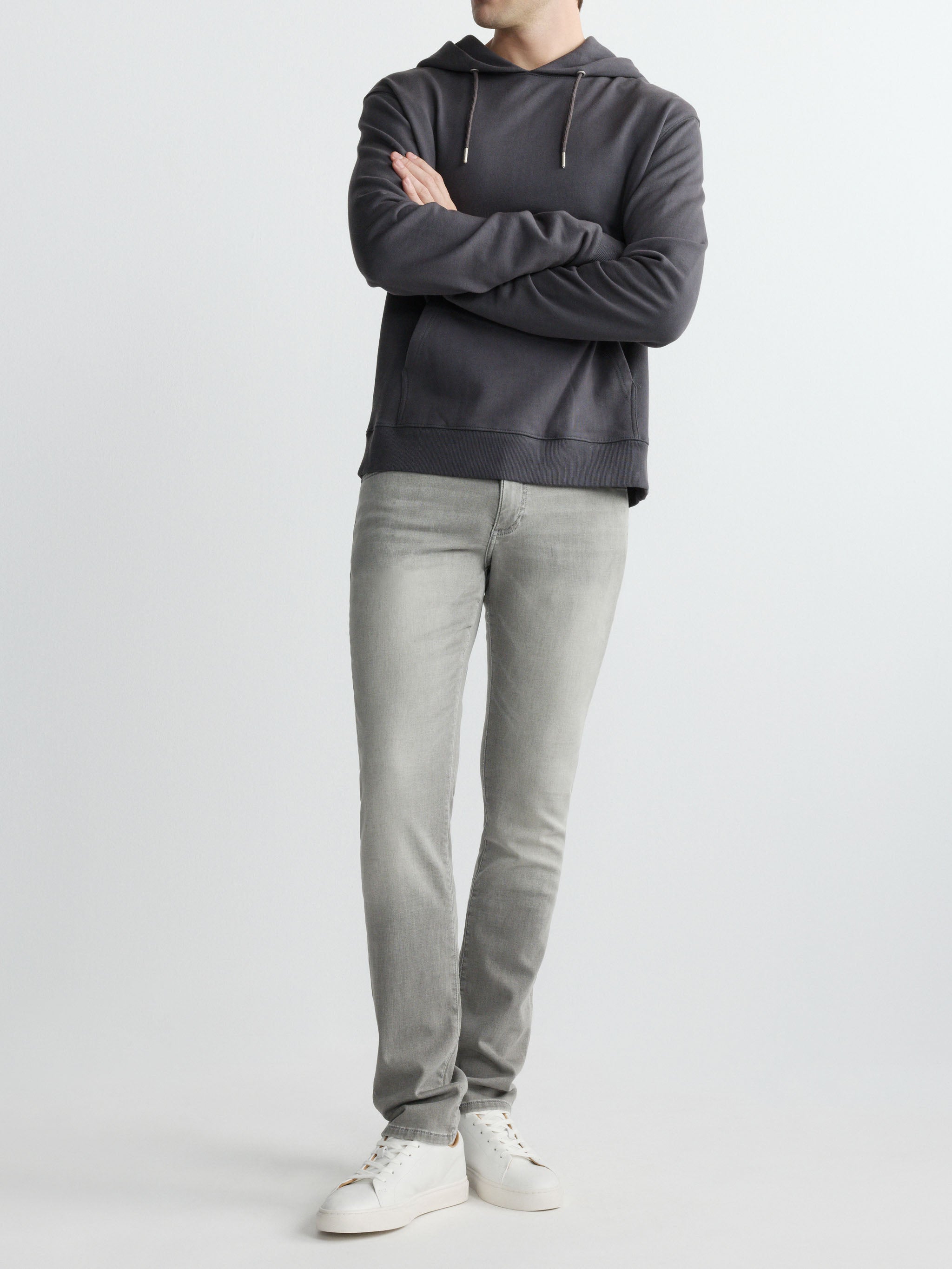 Person wearing a dark gray hoodie and light gray jeans on a white background