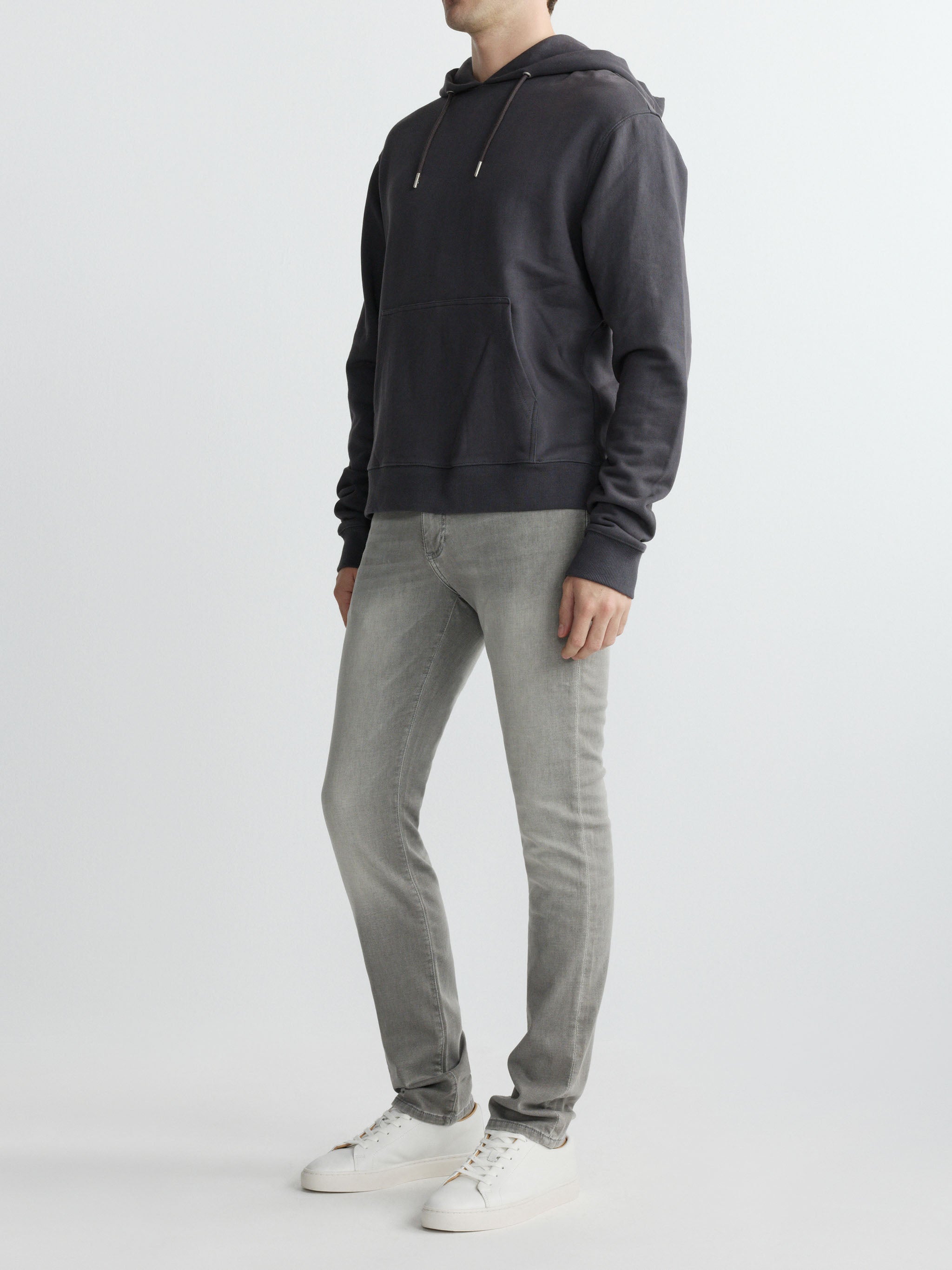 Person wearing a dark gray hoodie and light gray pants on a white background