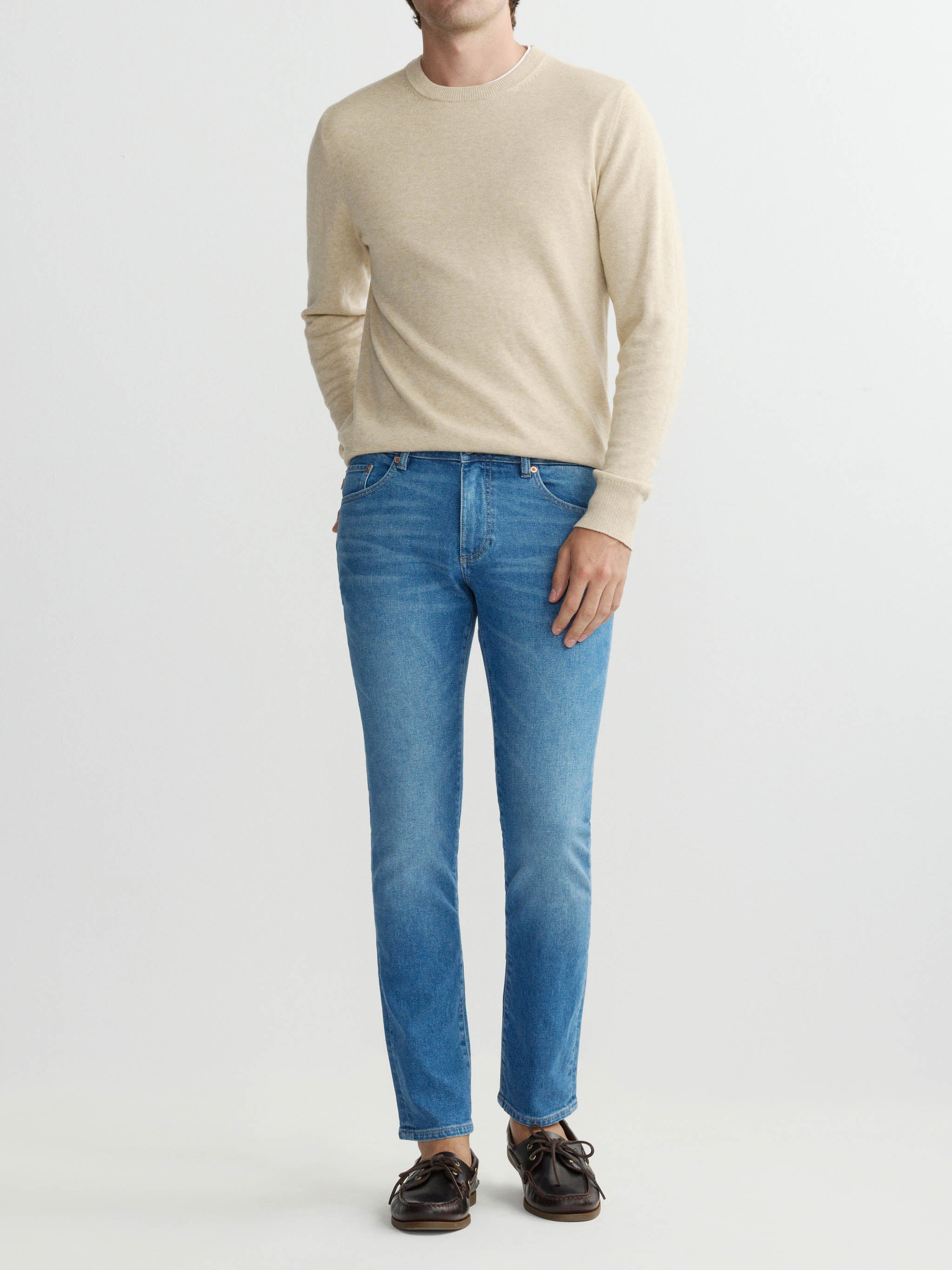 Person wearing a beige sweater and blue jeans on a white background