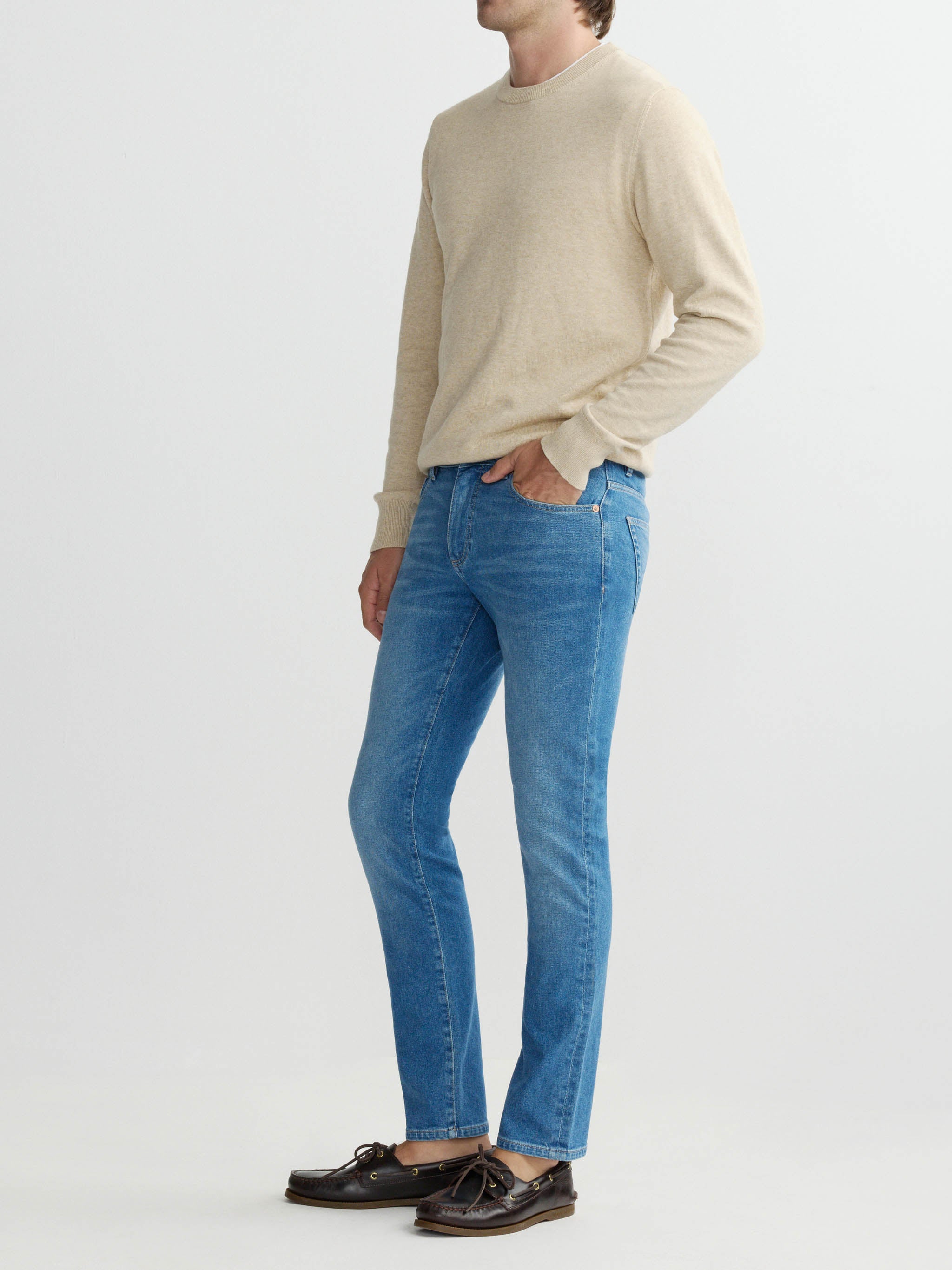 Person wearing a beige sweater and blue jeans on a white background