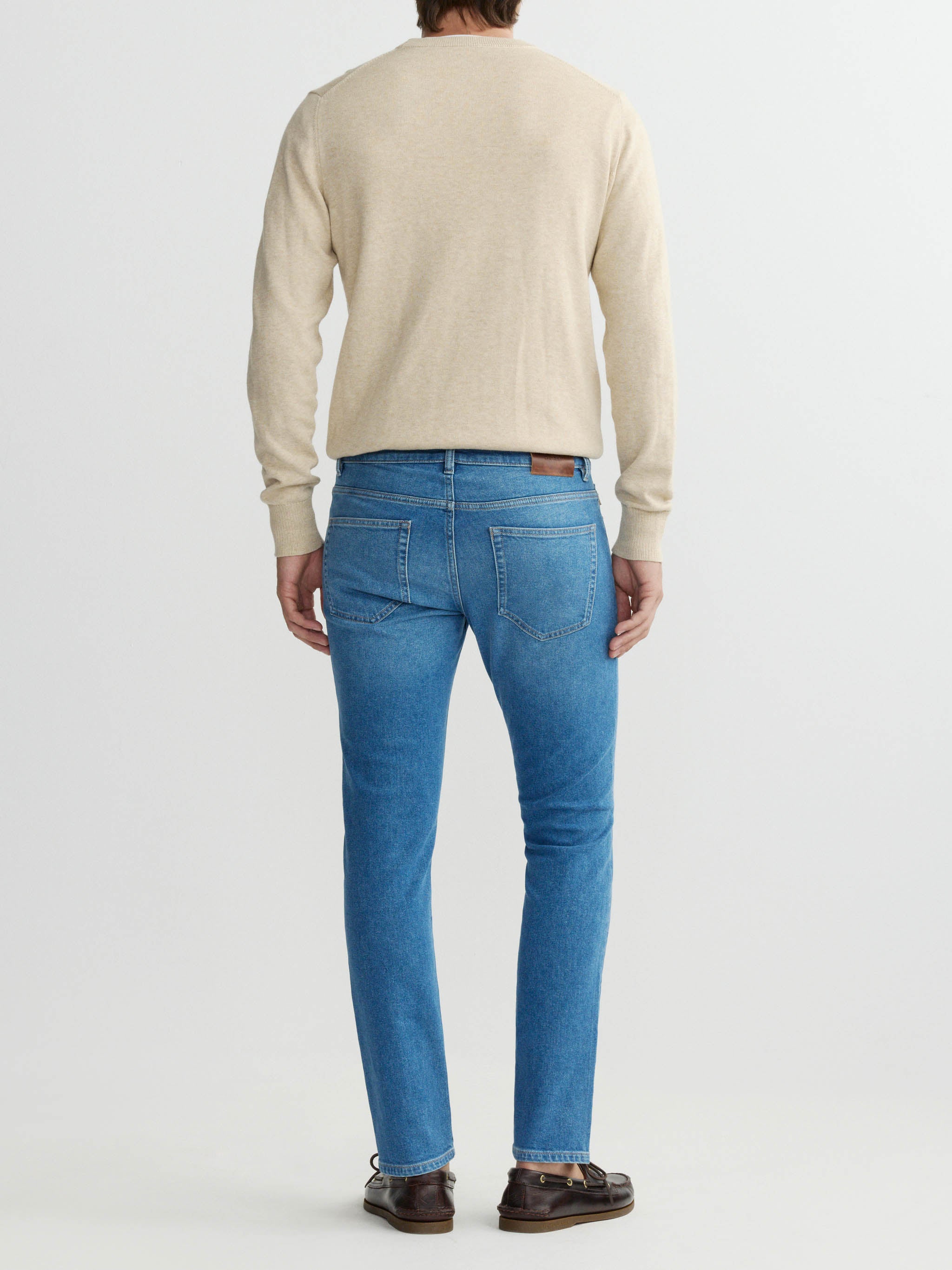 Person wearing a beige sweater and blue jeans on a white background