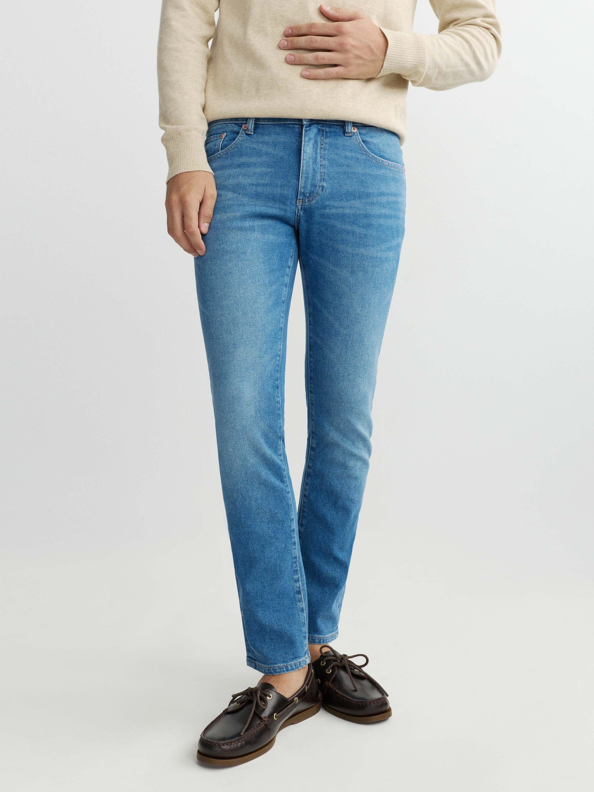 Person wearing blue jeans and a beige sweater on a white background