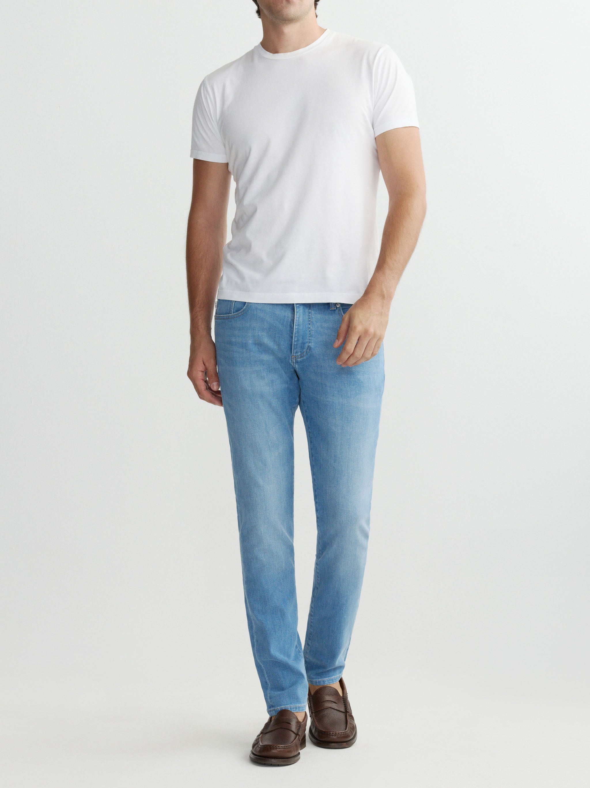 Person wearing a white t-shirt and light blue jeans on a plain background