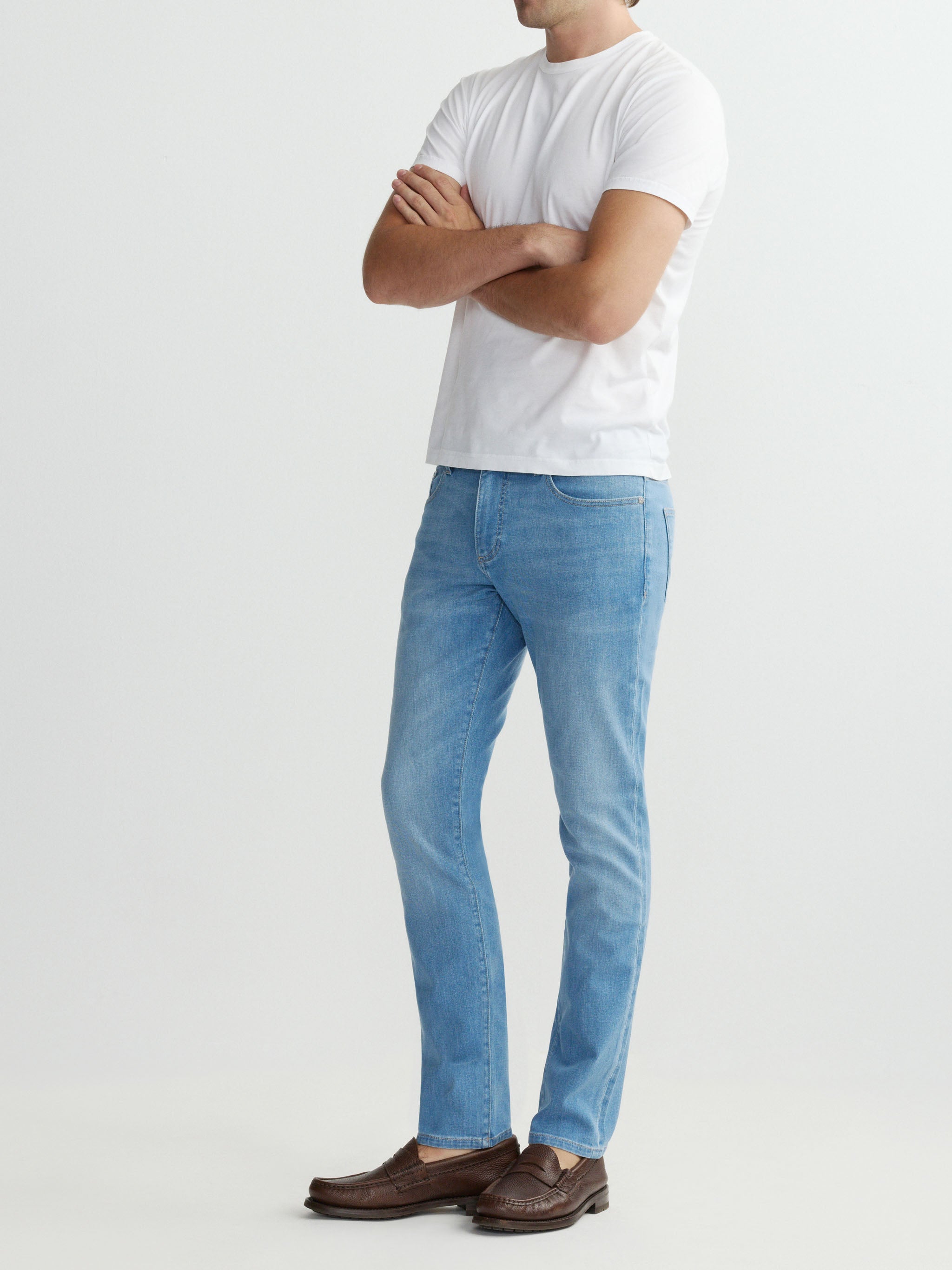 Person wearing light blue jeans and a white t-shirt on a plain background