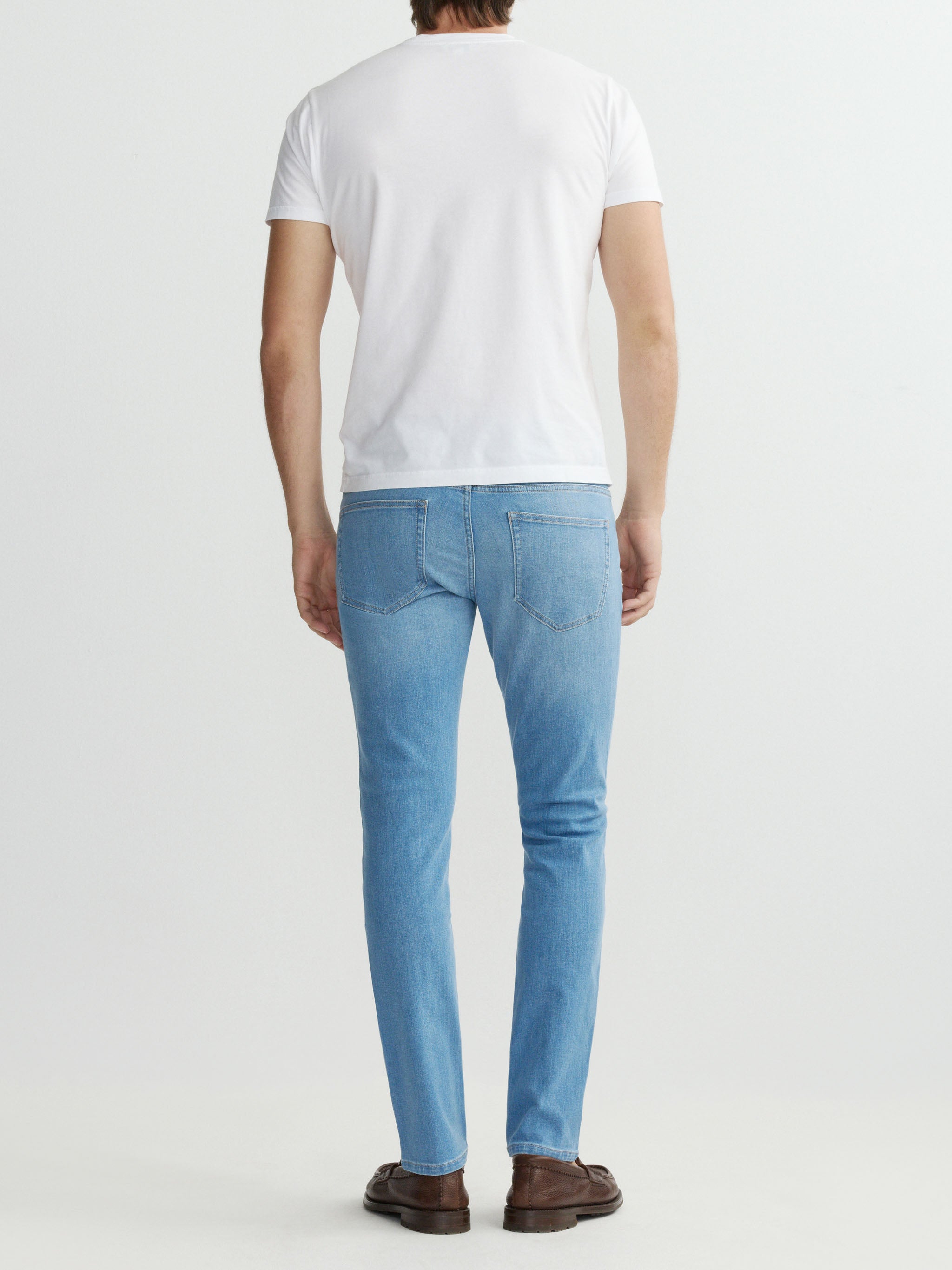 Person wearing light blue jeans and a white t-shirt on a plain background