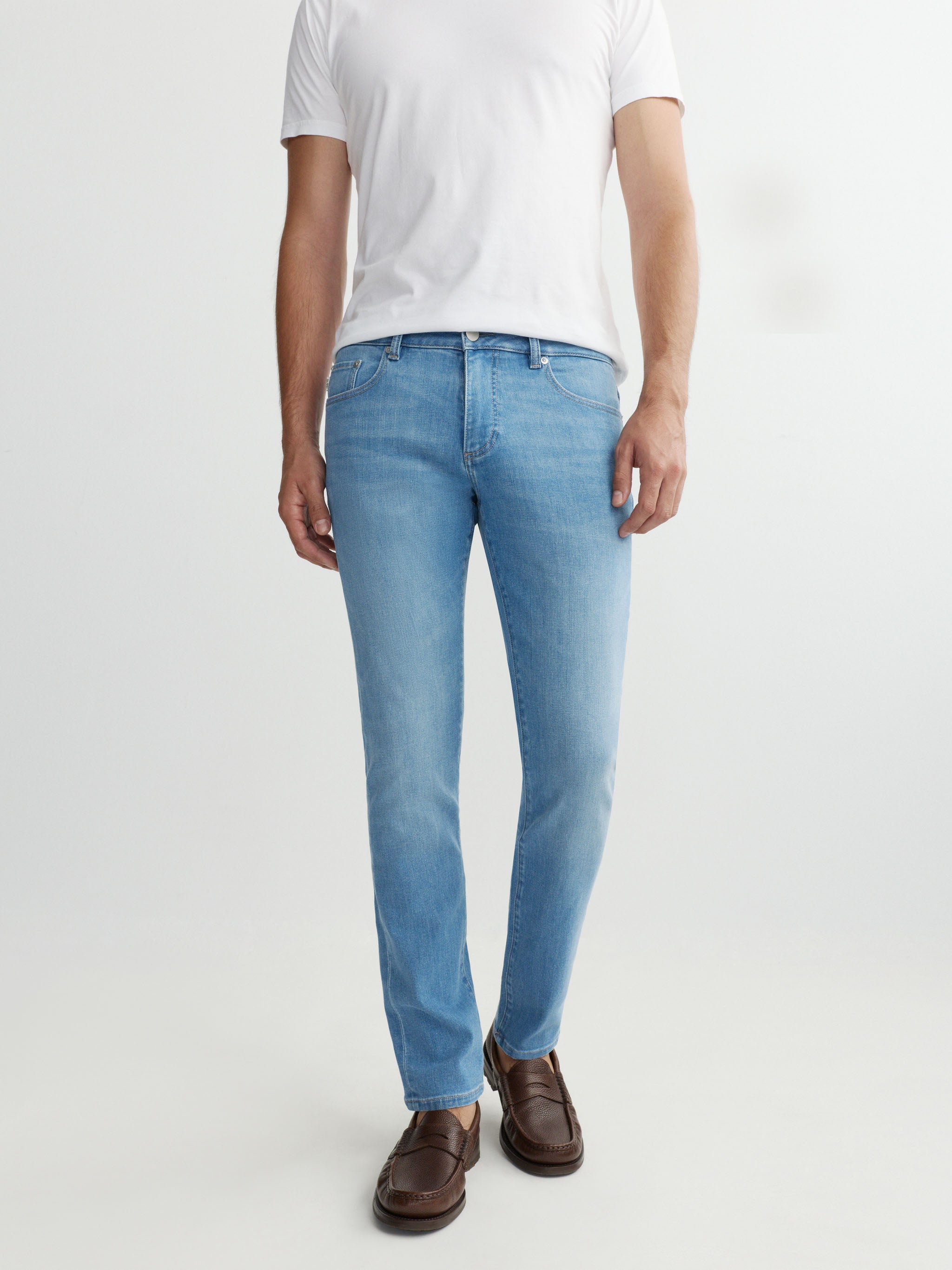 Person wearing light blue jeans and a white shirt on a white background
