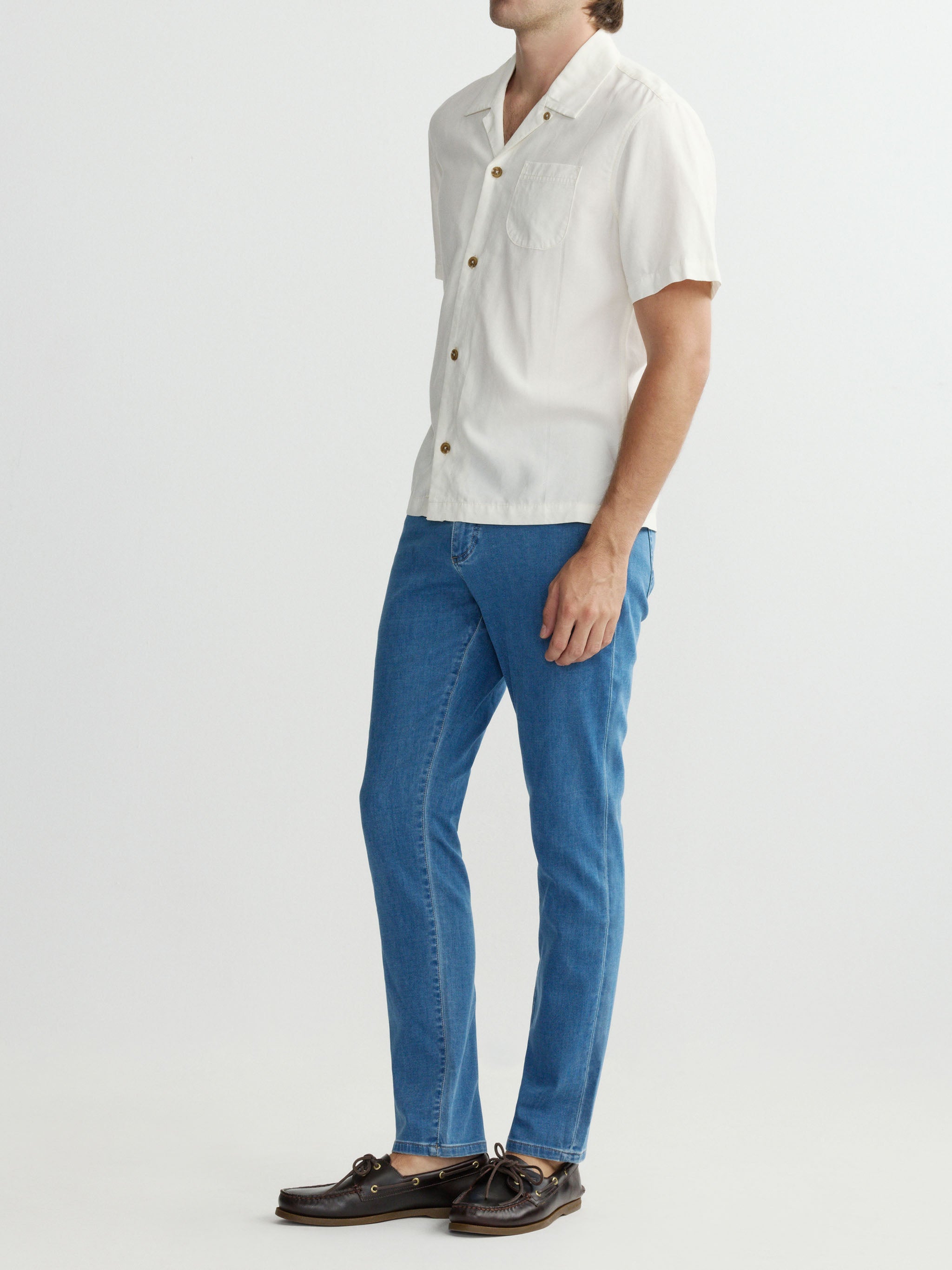 Person wearing a white shirt and blue jeans on a plain background