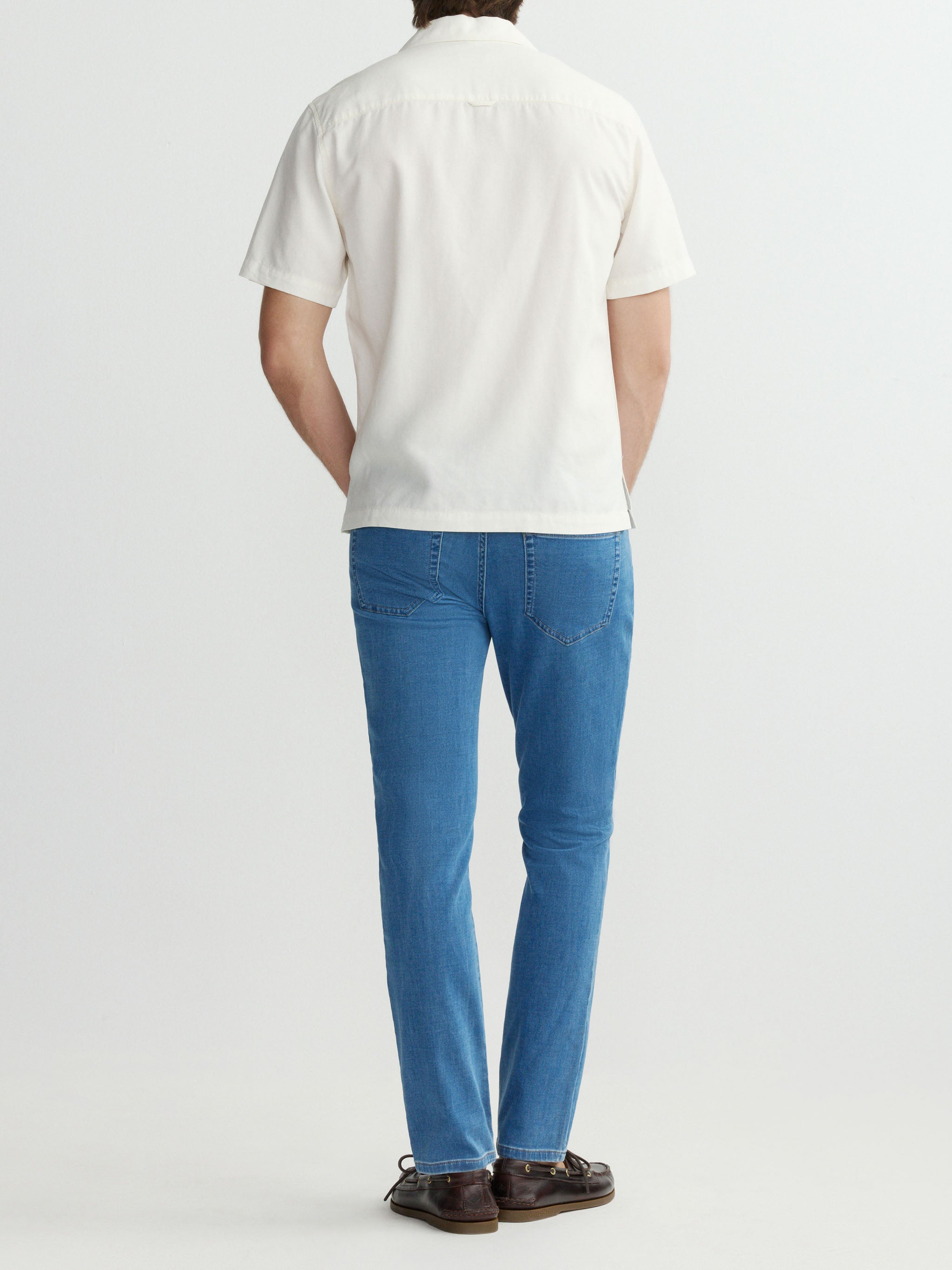 Person wearing a white polo shirt and blue jeans on a white background