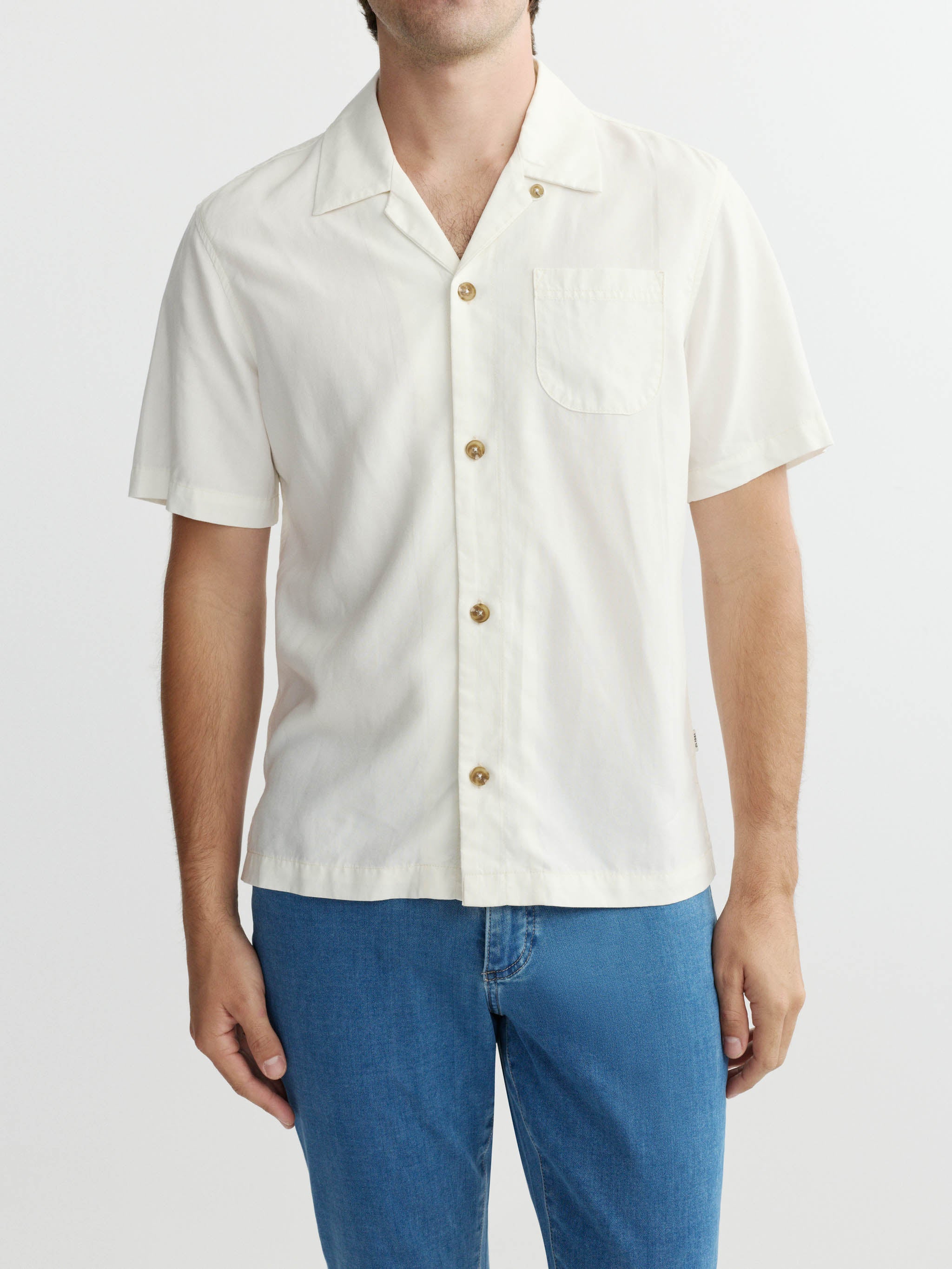 Person wearing a white short-sleeve shirt with gold buttons on a plain background