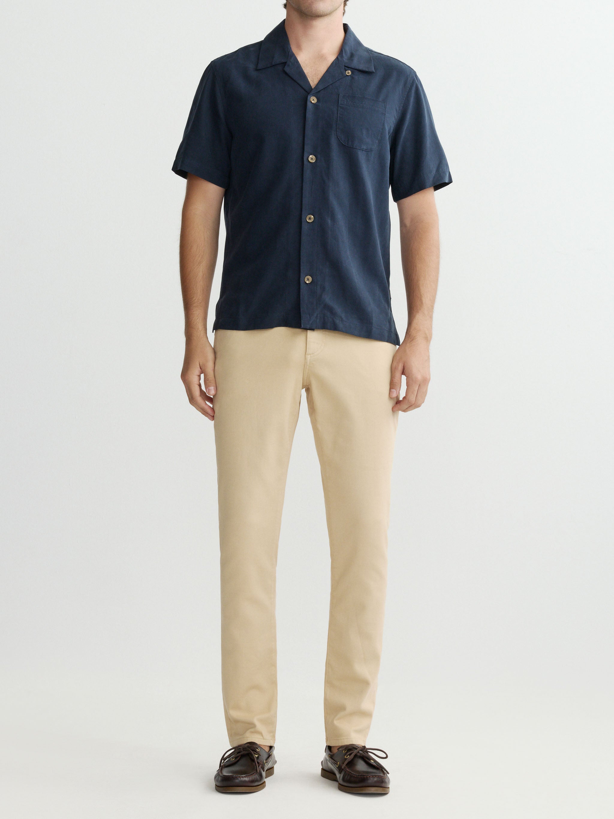 Person wearing a navy short-sleeve shirt and beige pants on a white background