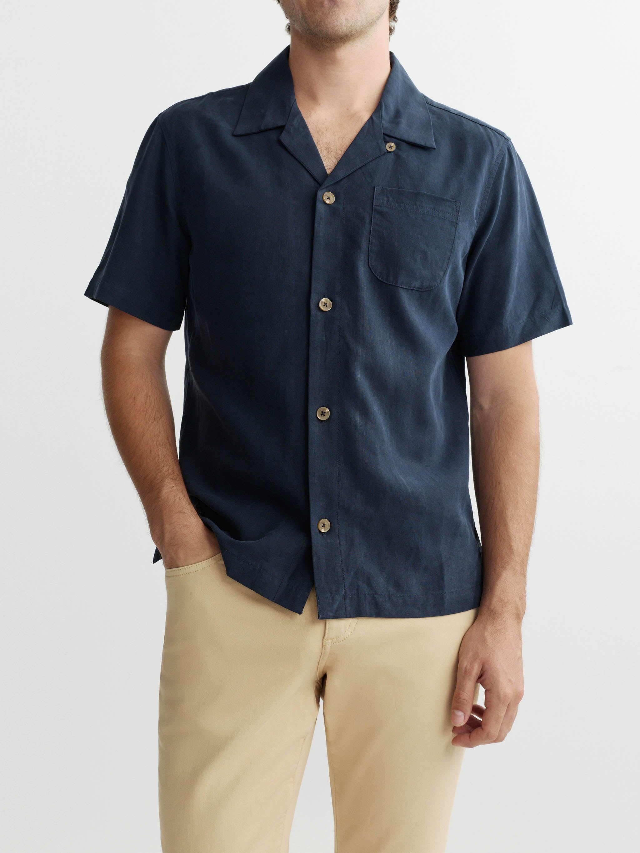Man wearing a navy short-sleeve shirt with beige pants on a white background