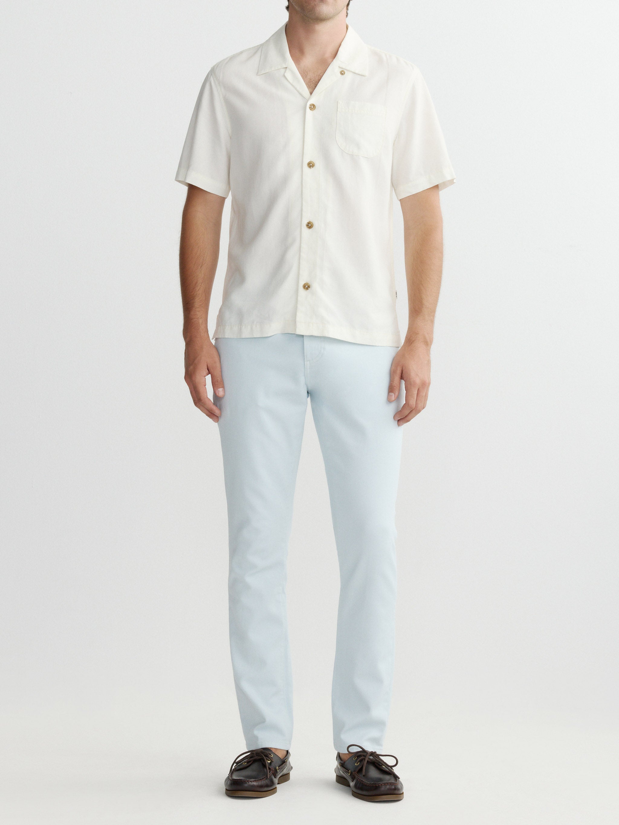 Man wearing a white button-up shirt and light blue pants on a white background