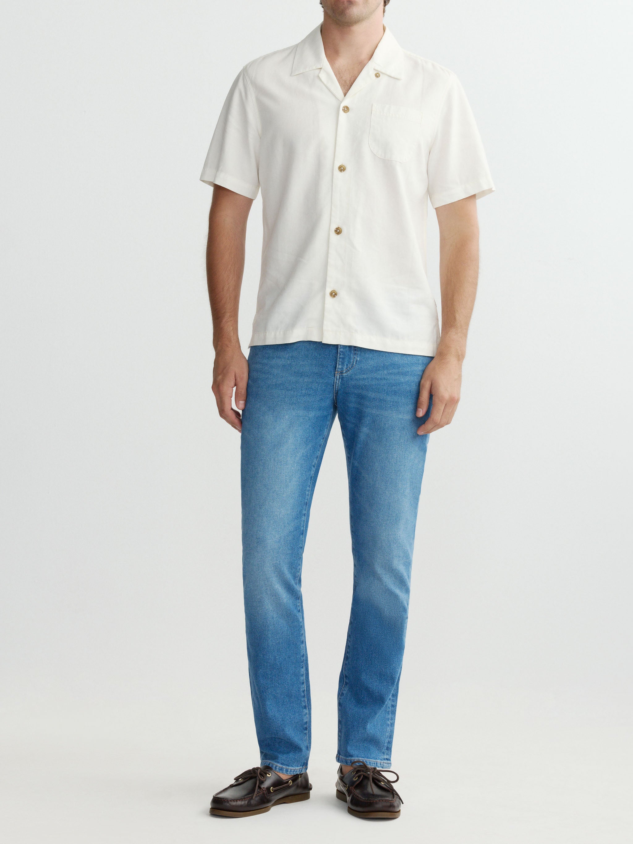 Man wearing a white button-up shirt and blue jeans on a white background