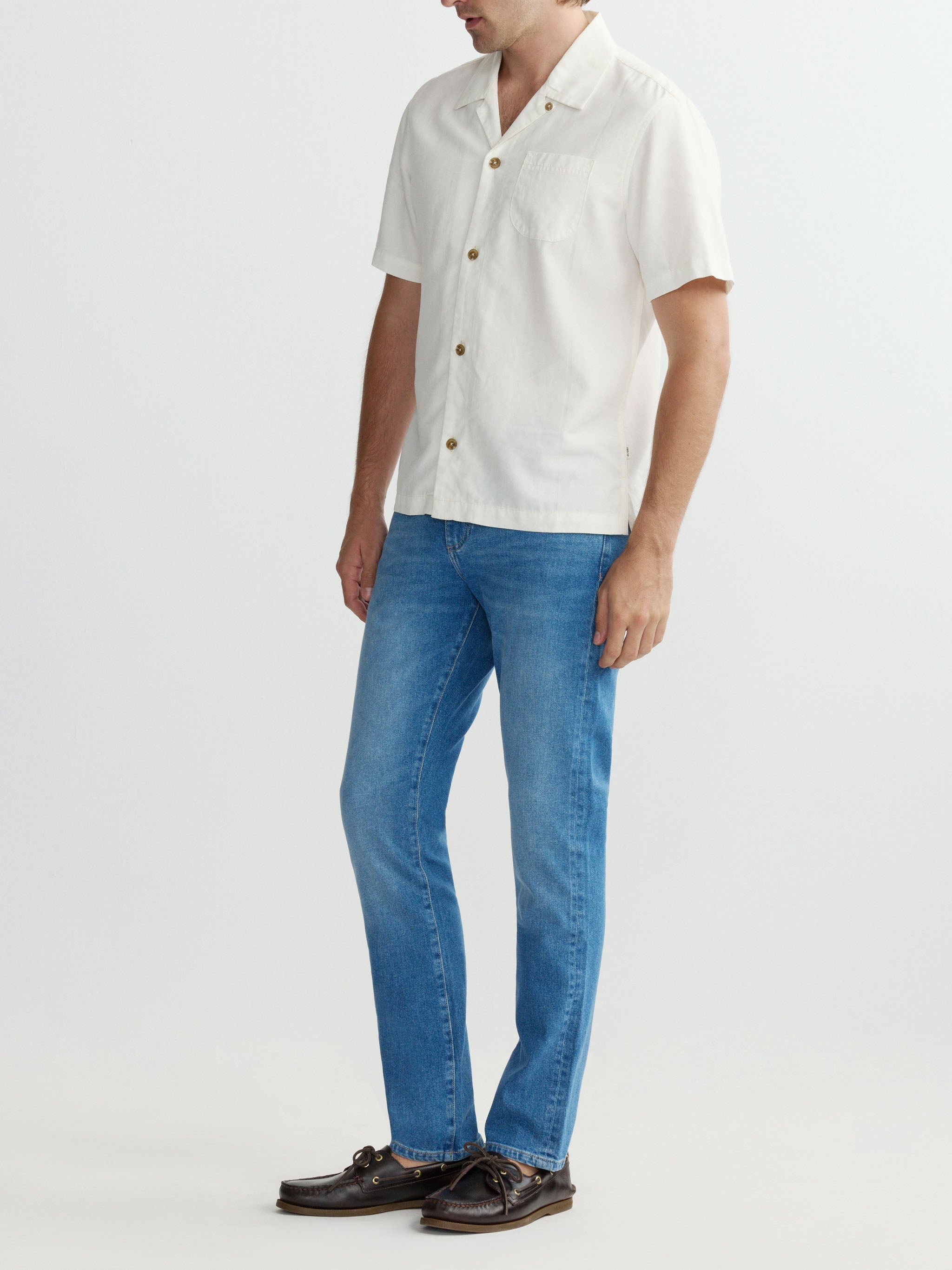 Person wearing a white shirt, blue jeans, and brown shoes on a light gray background