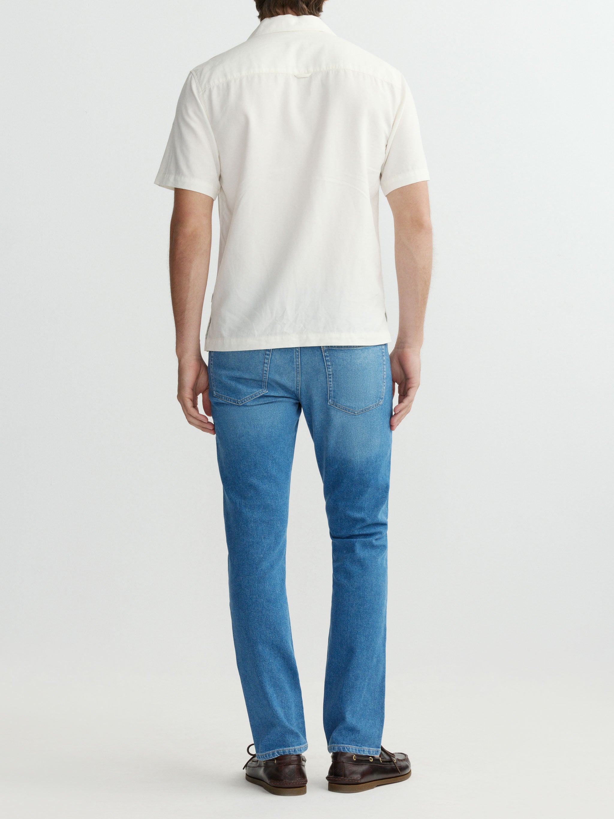Person wearing a white polo shirt and blue jeans on a plain background