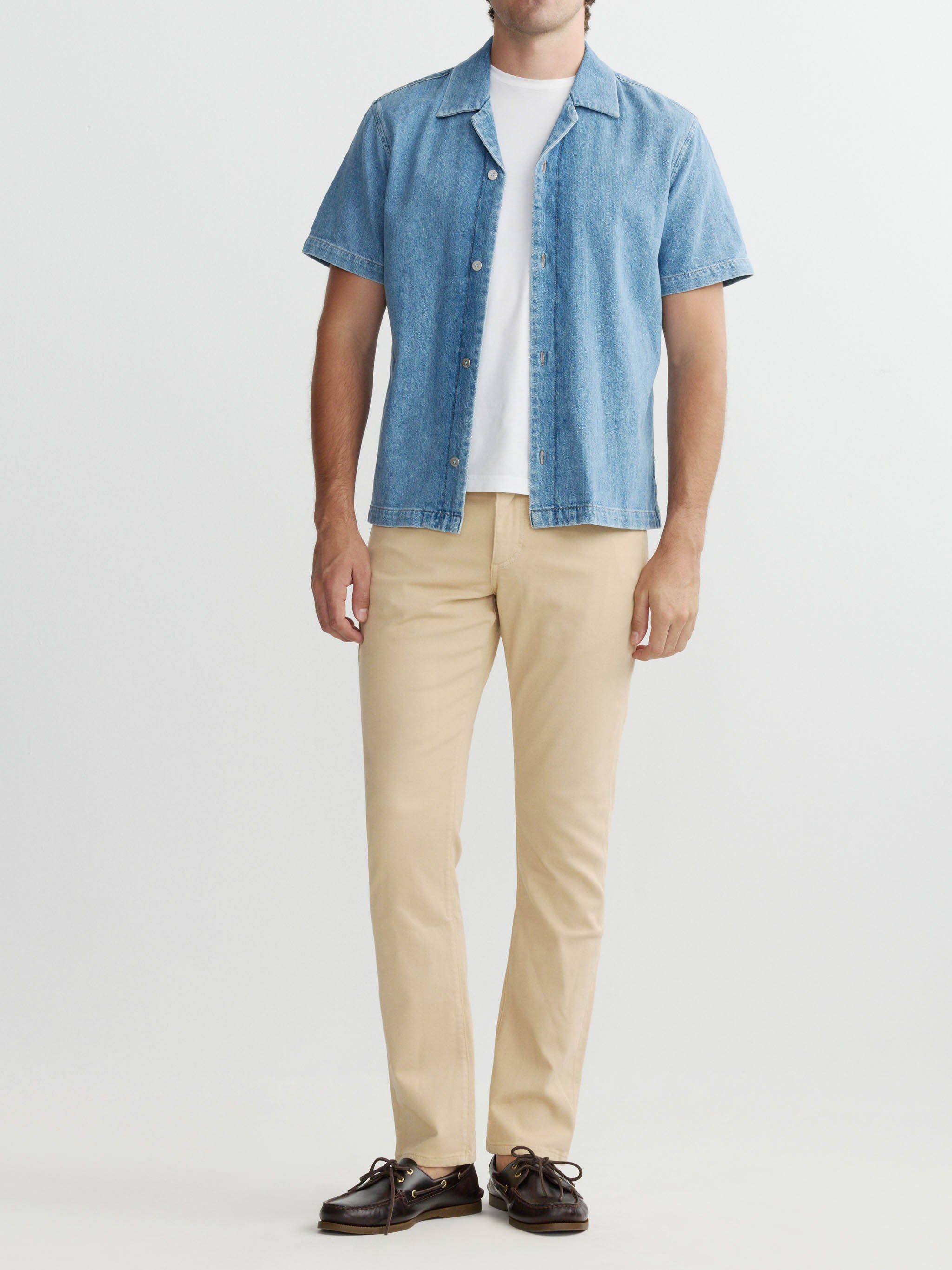 Man wearing a blue denim shirt over a white t-shirt with beige pants on a white background