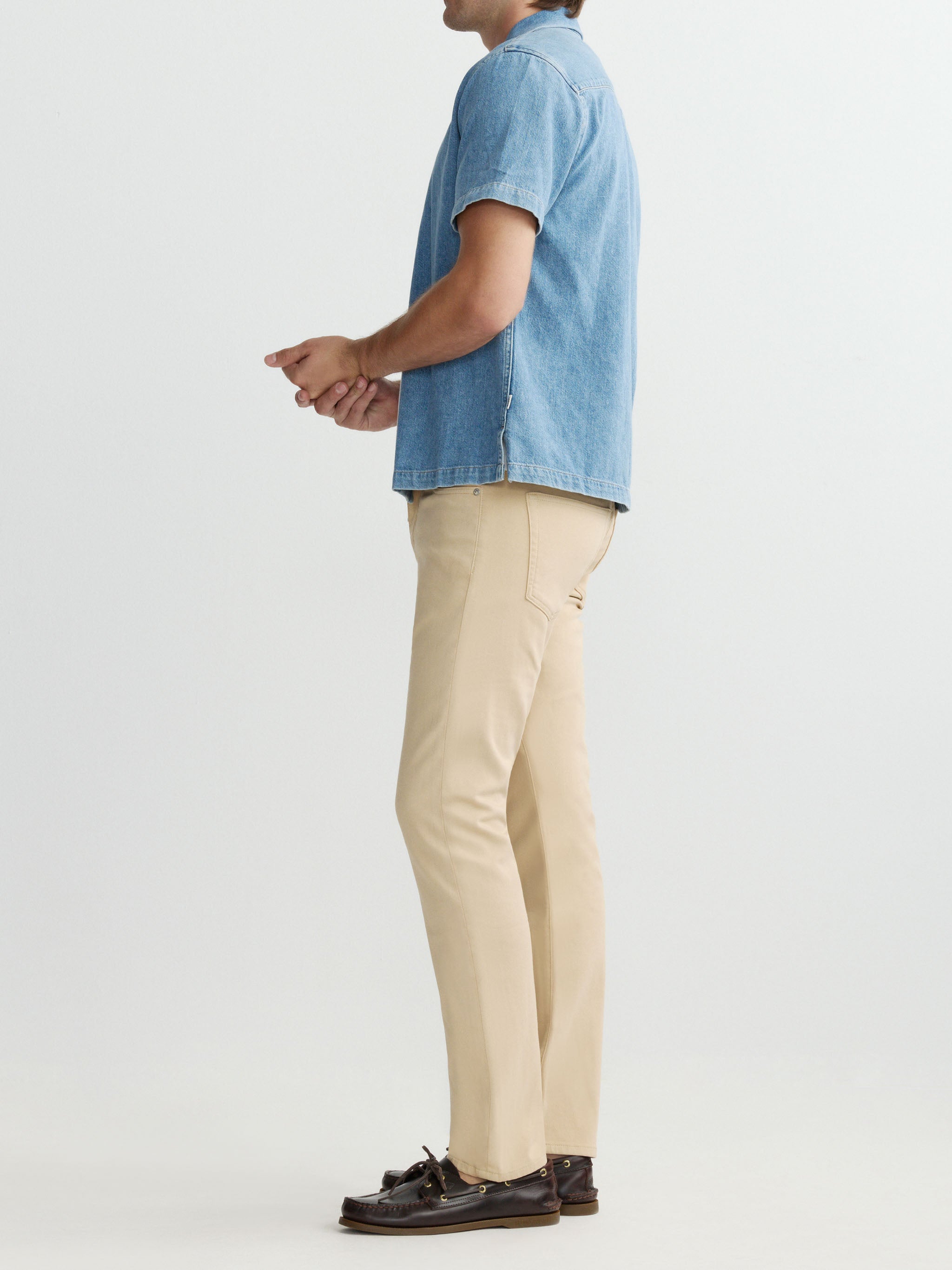 Person wearing a blue denim shirt and beige pants on a white background
