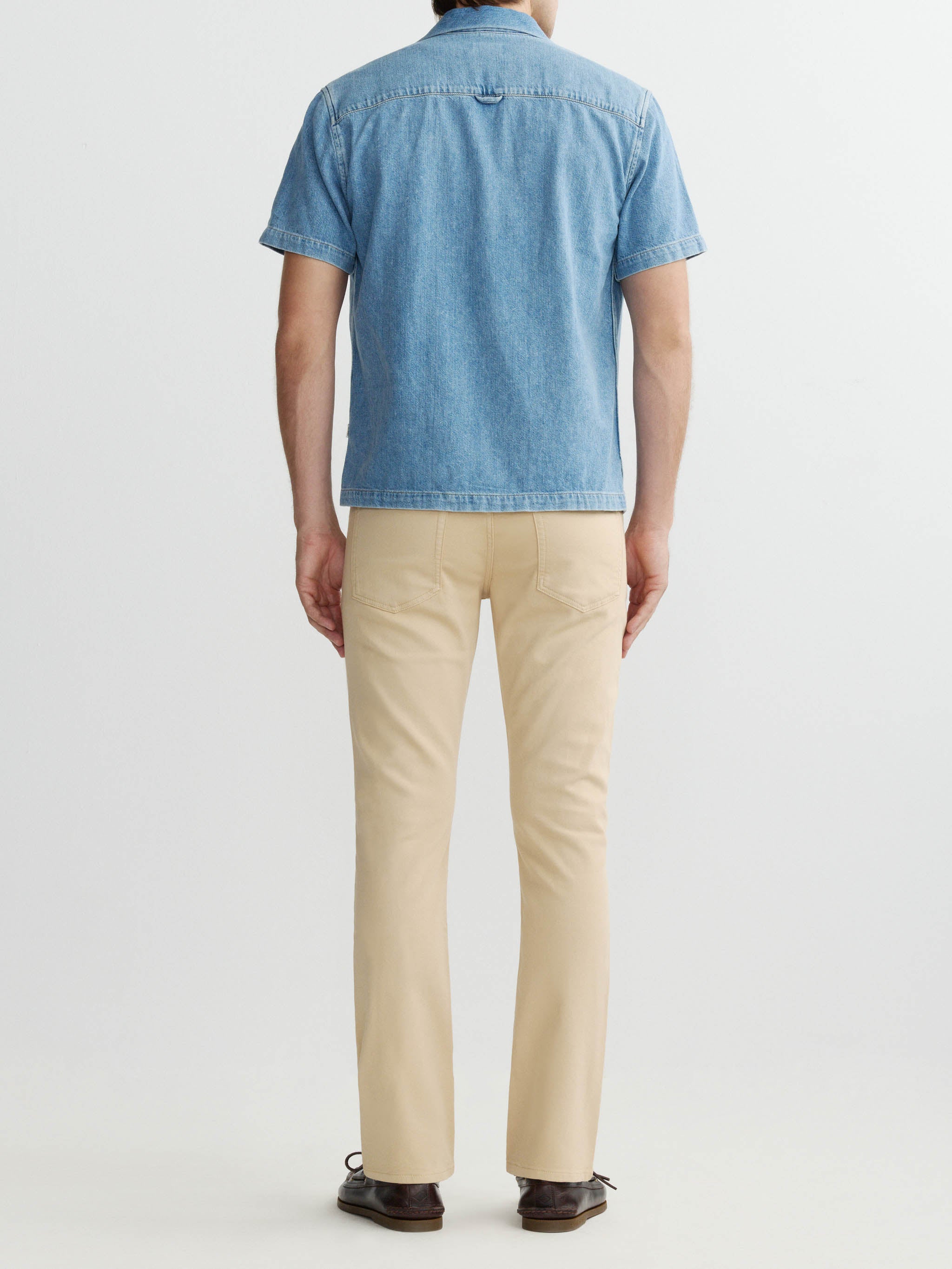 Person wearing a blue denim shirt and beige pants on a white background