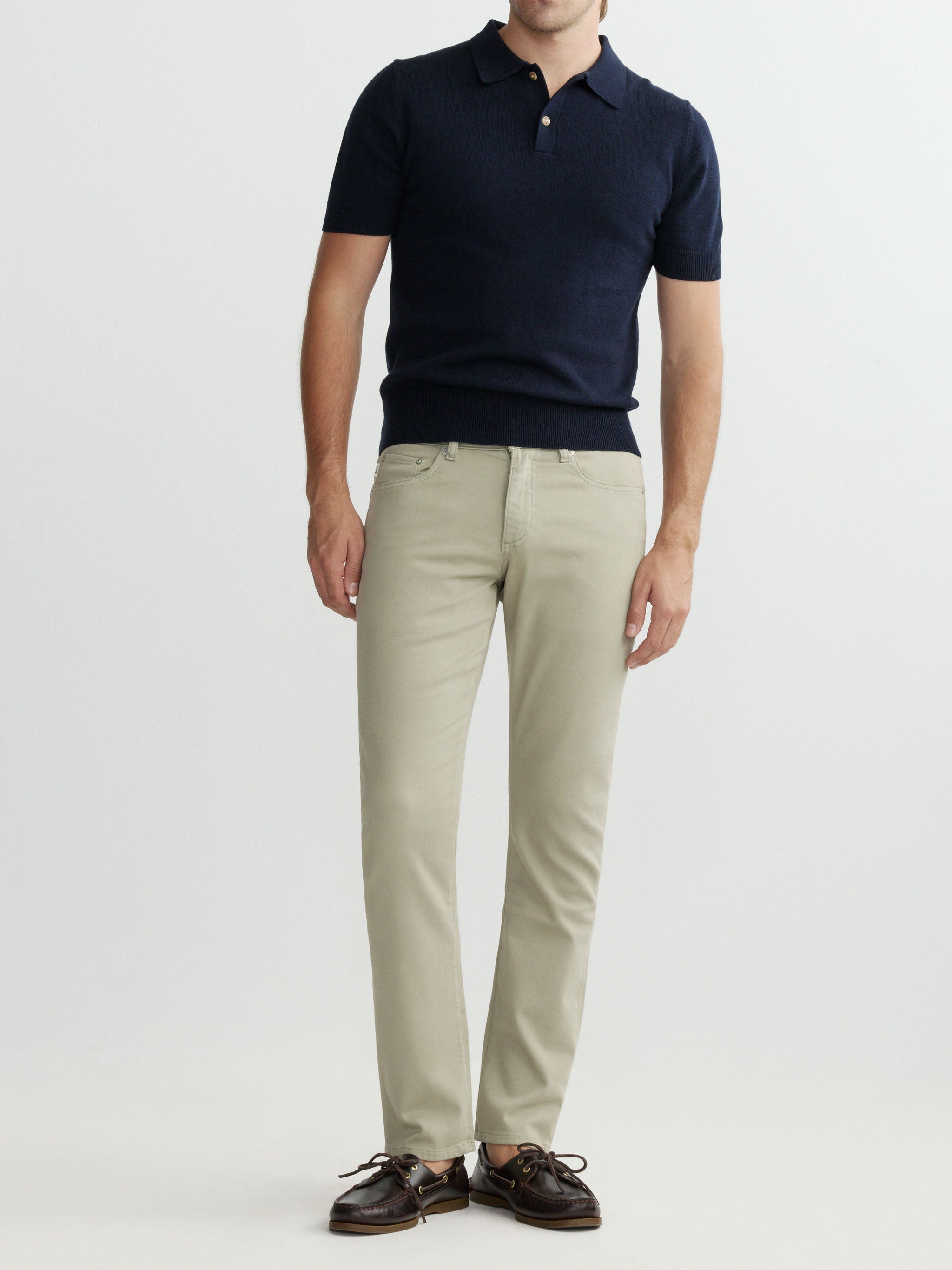 Man wearing a navy polo shirt and beige pants on a white background