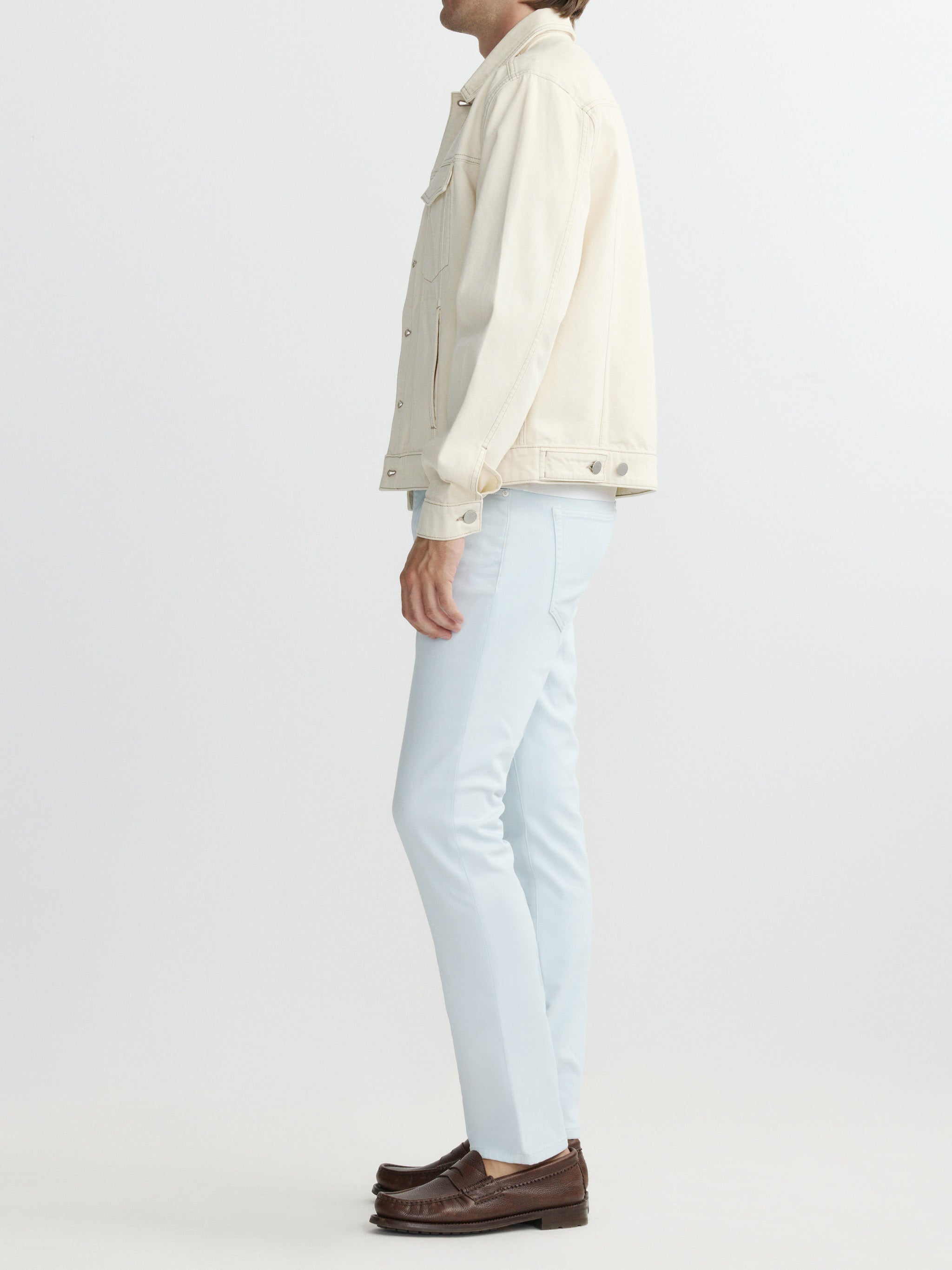 Person wearing a light-colored jacket and light blue jeans on a white background