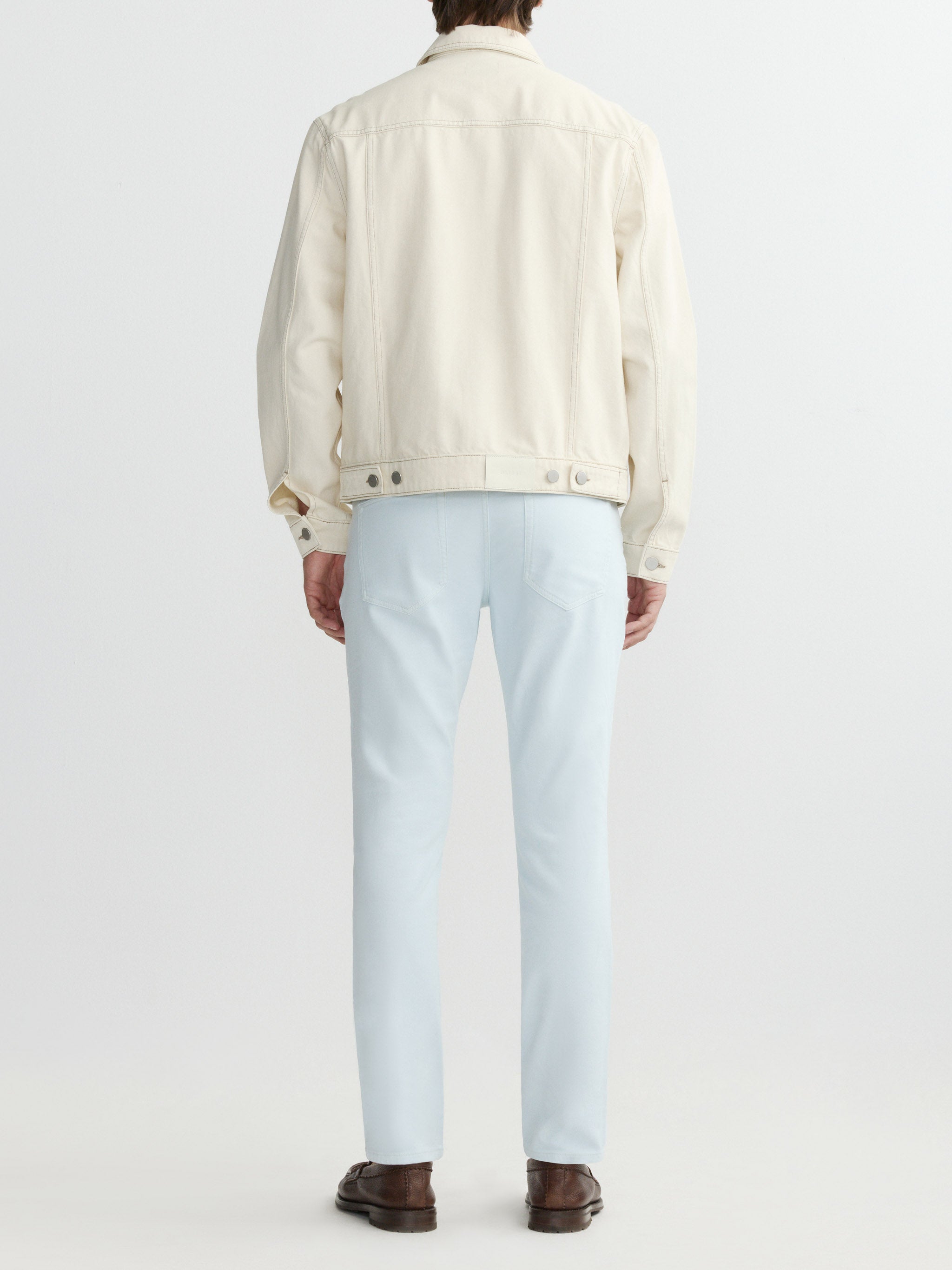 Person wearing a cream jacket and light blue jeans on a white background