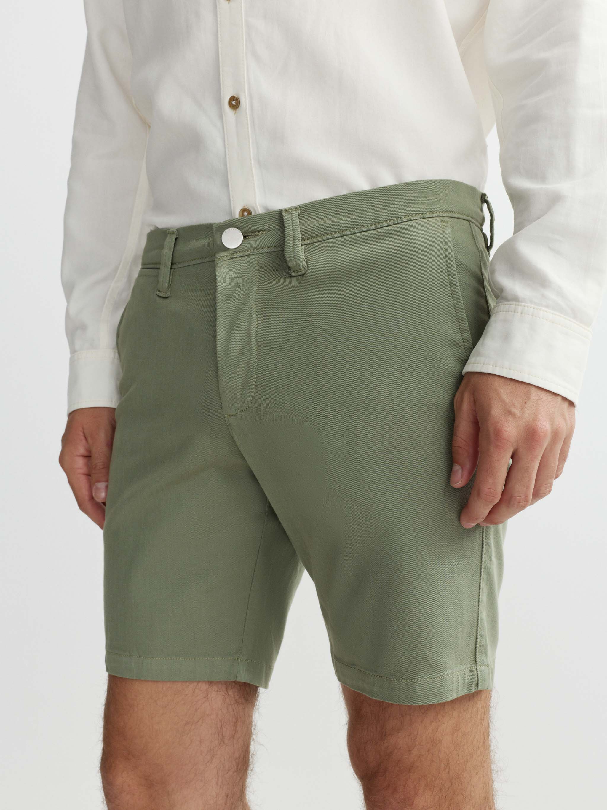 Person wearing green shorts and a white shirt on a plain background