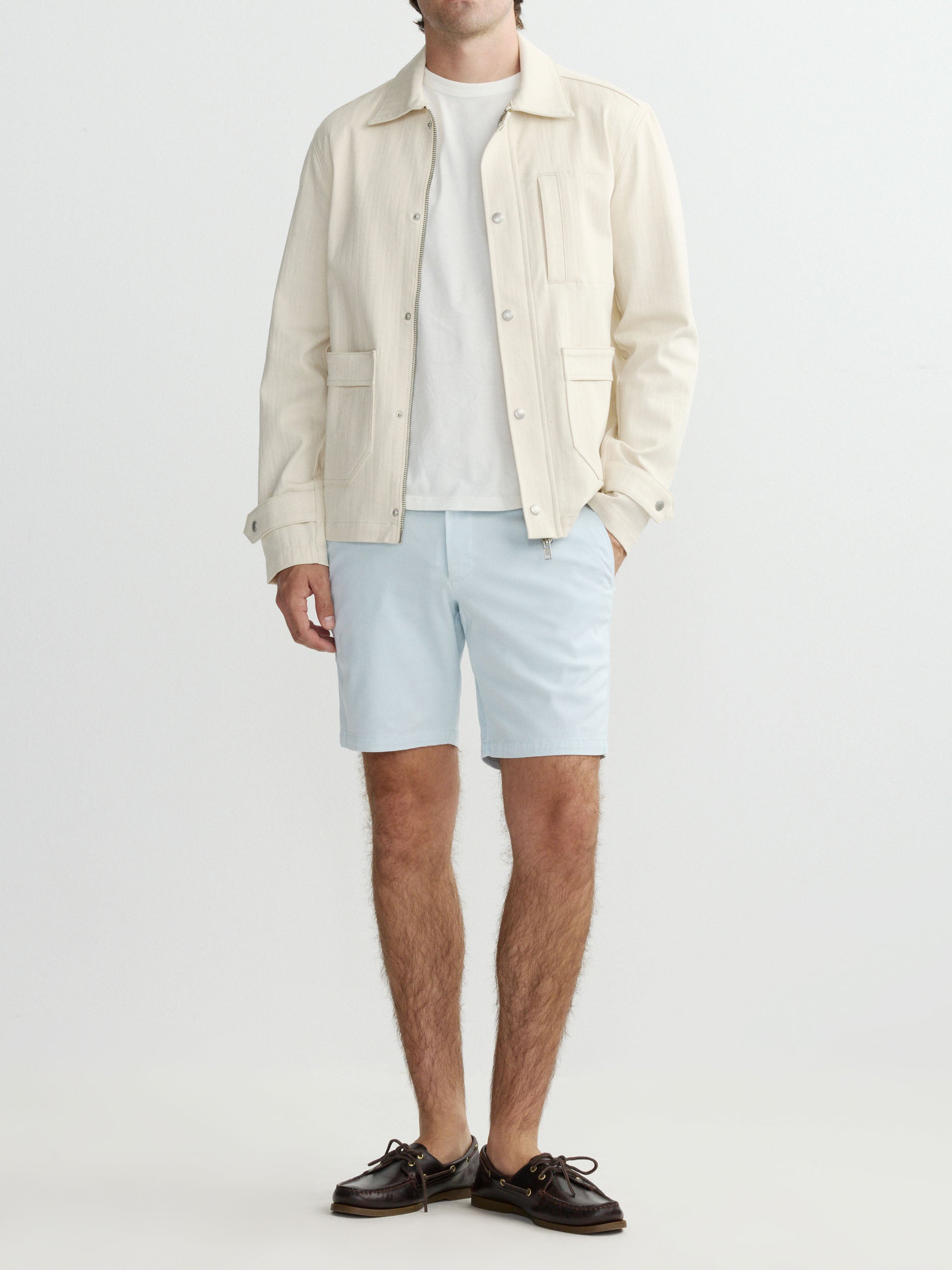 Man wearing a light-colored shirt, shorts, and jacket on a white background
