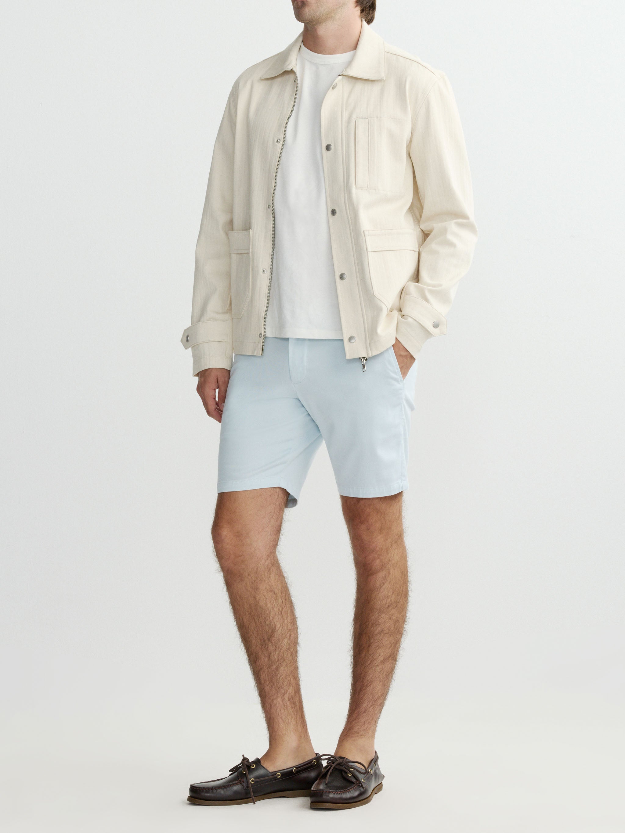Man wearing a beige jacket, white t-shirt, light blue shorts, and brown shoes on a white background