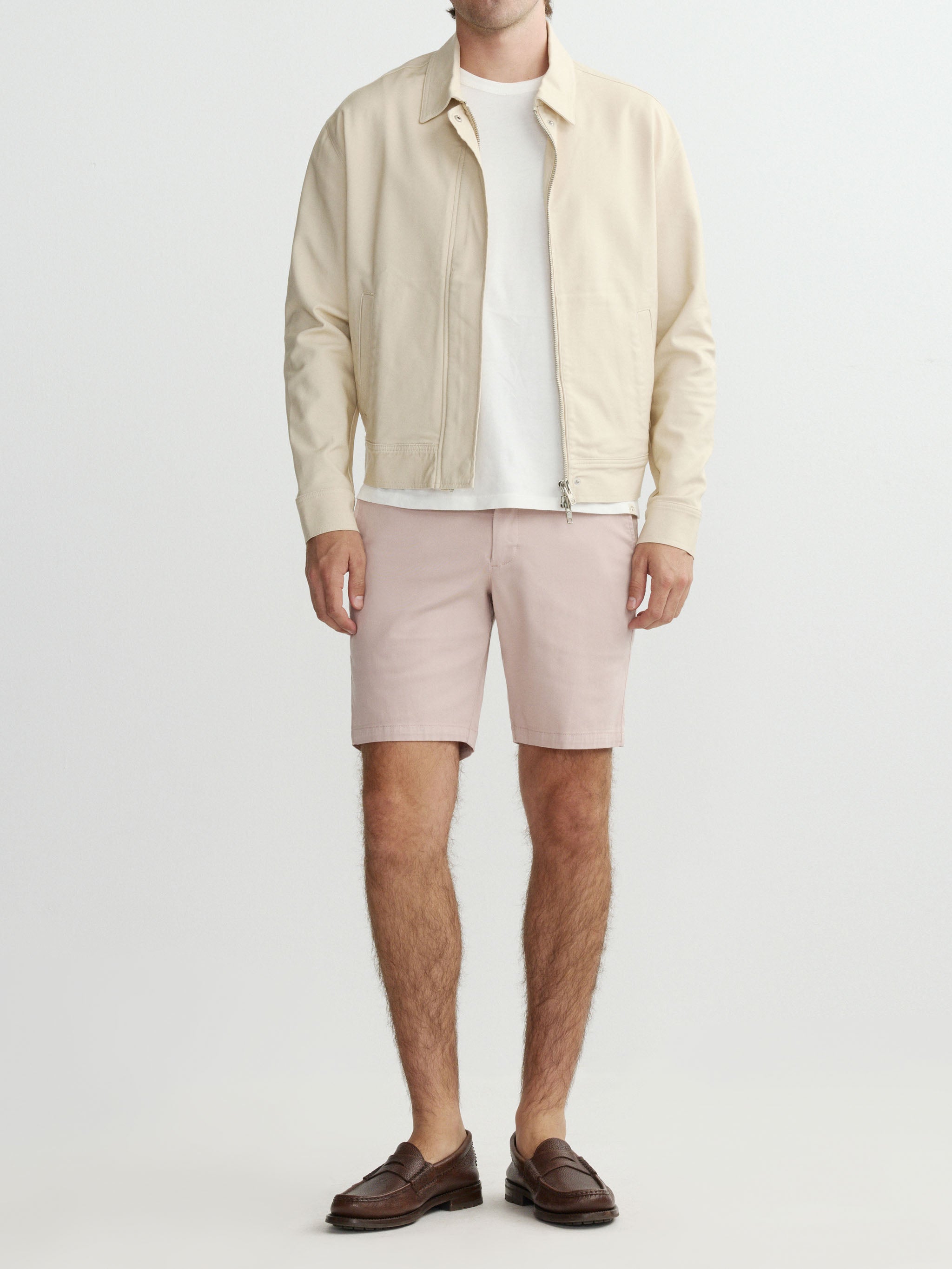 Man wearing a beige jacket, white shirt, and pink shorts on a light gray background